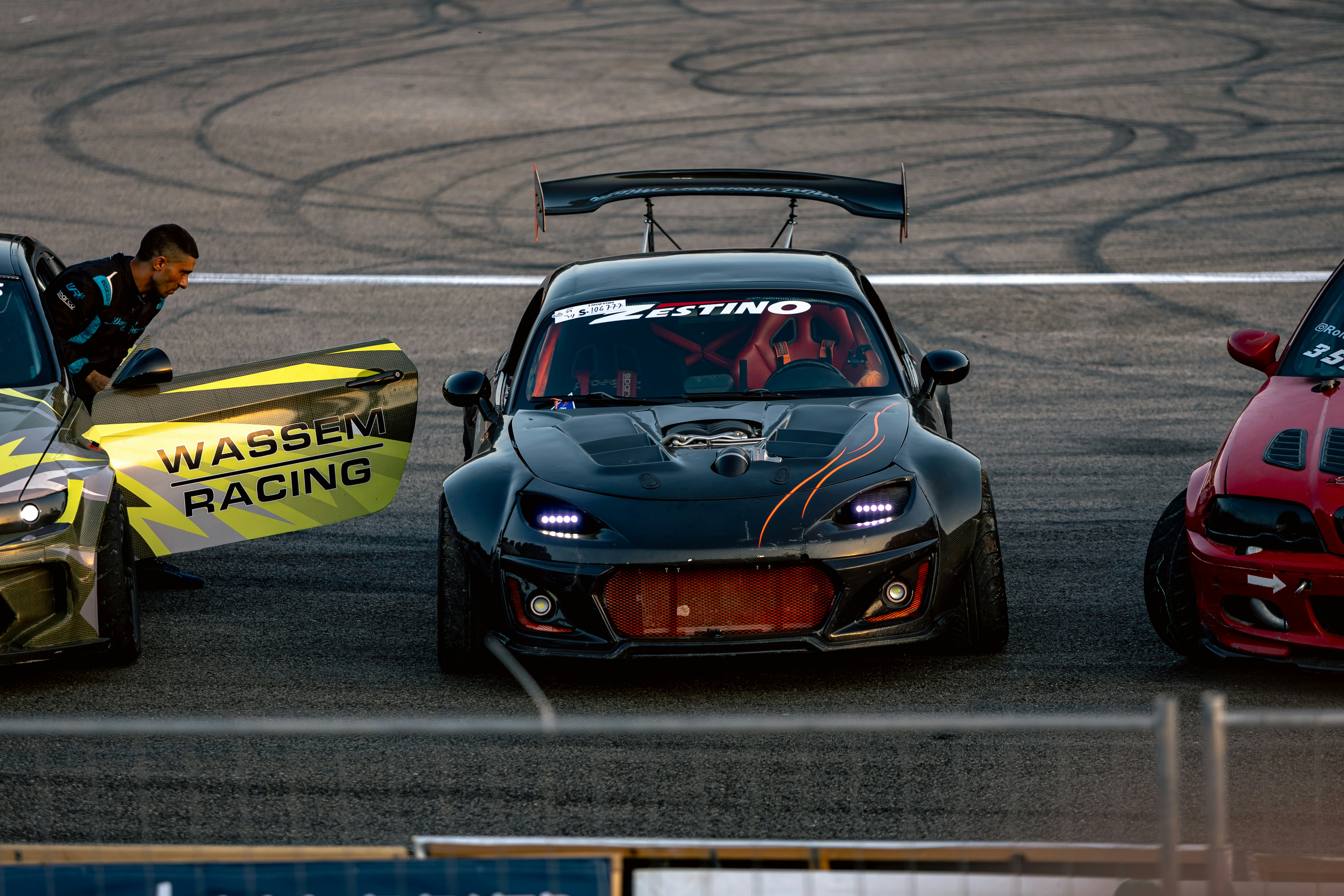 A person exiting a drift car on a track with other race cars