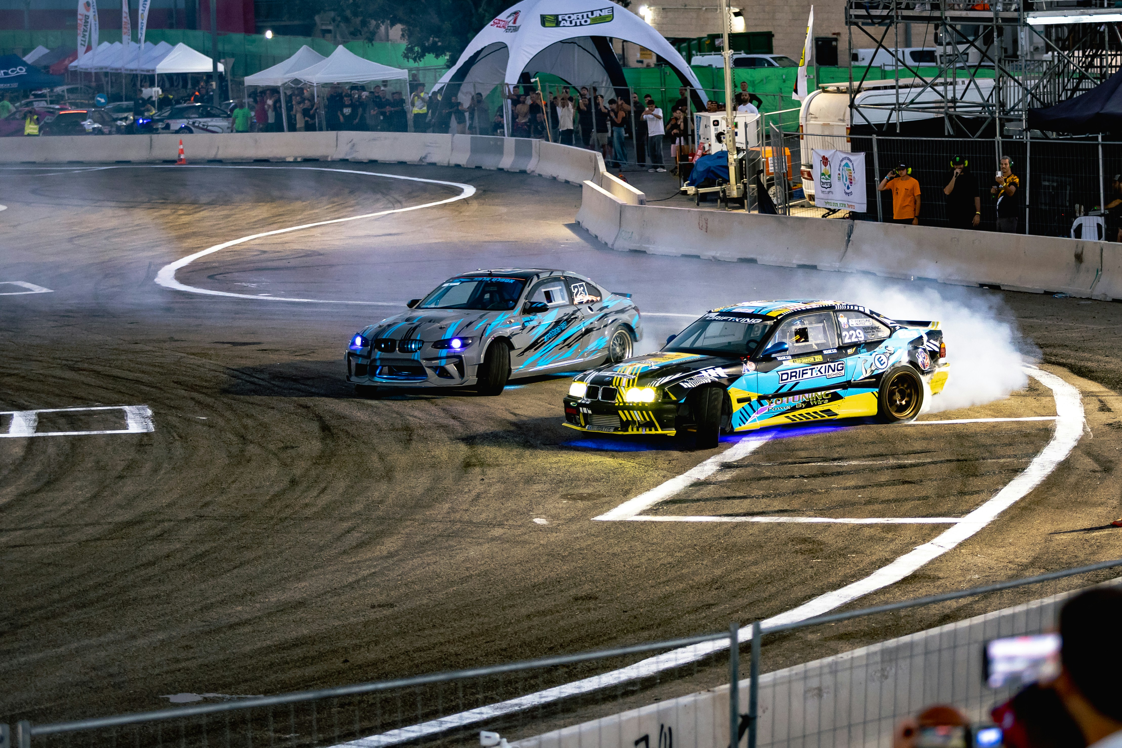 Two modified BMW drift cars racing on a track with smoke from tires