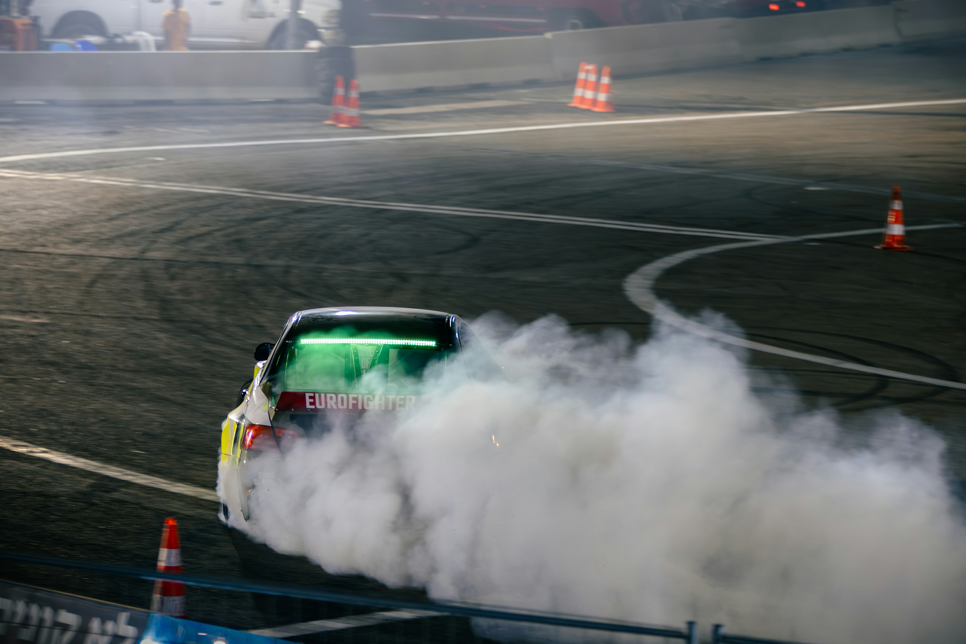 A car drifting on a track with thick white smoke and orange traffic cones
