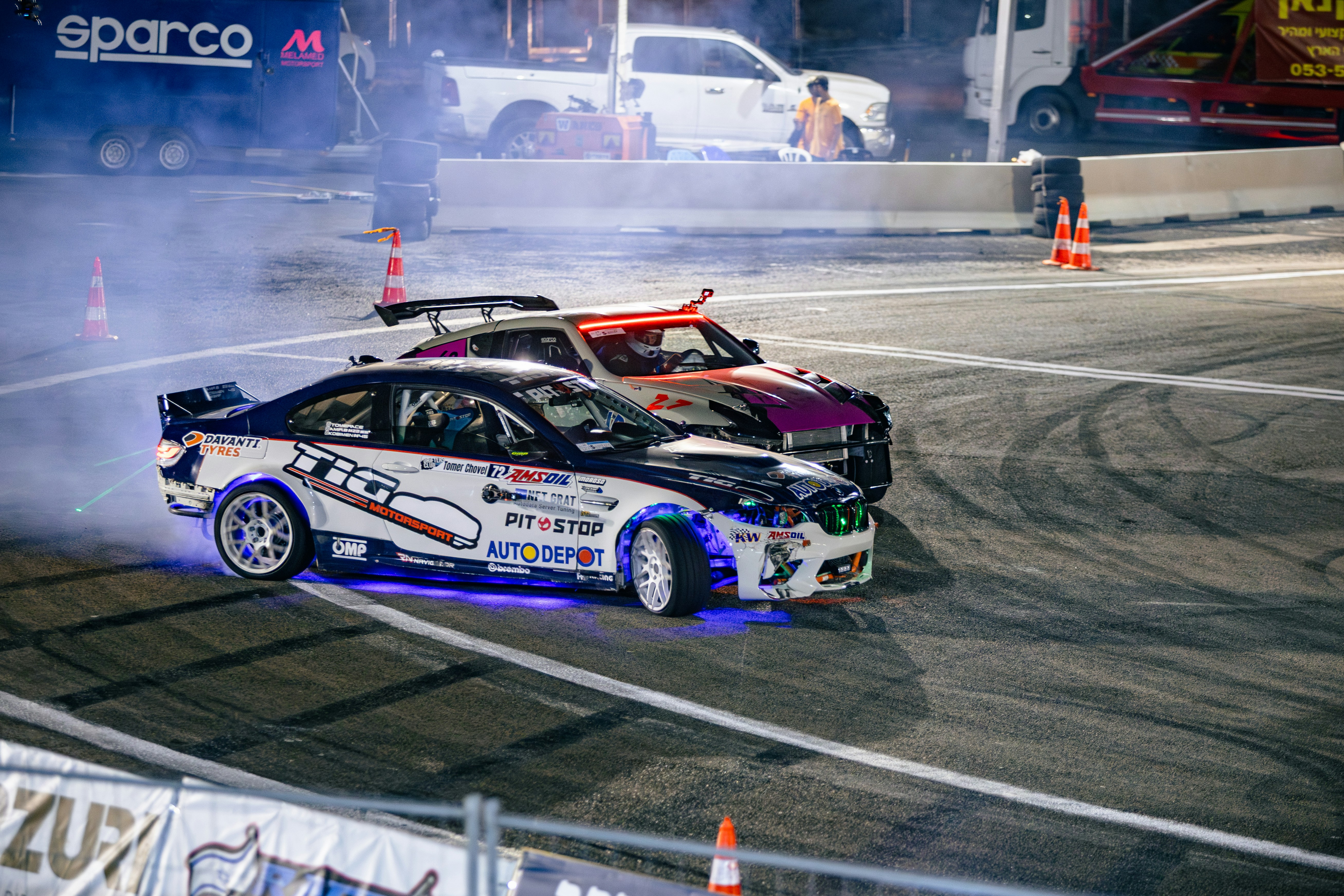 Two drift cars with underglow lighting performing a drift on an asphalt track