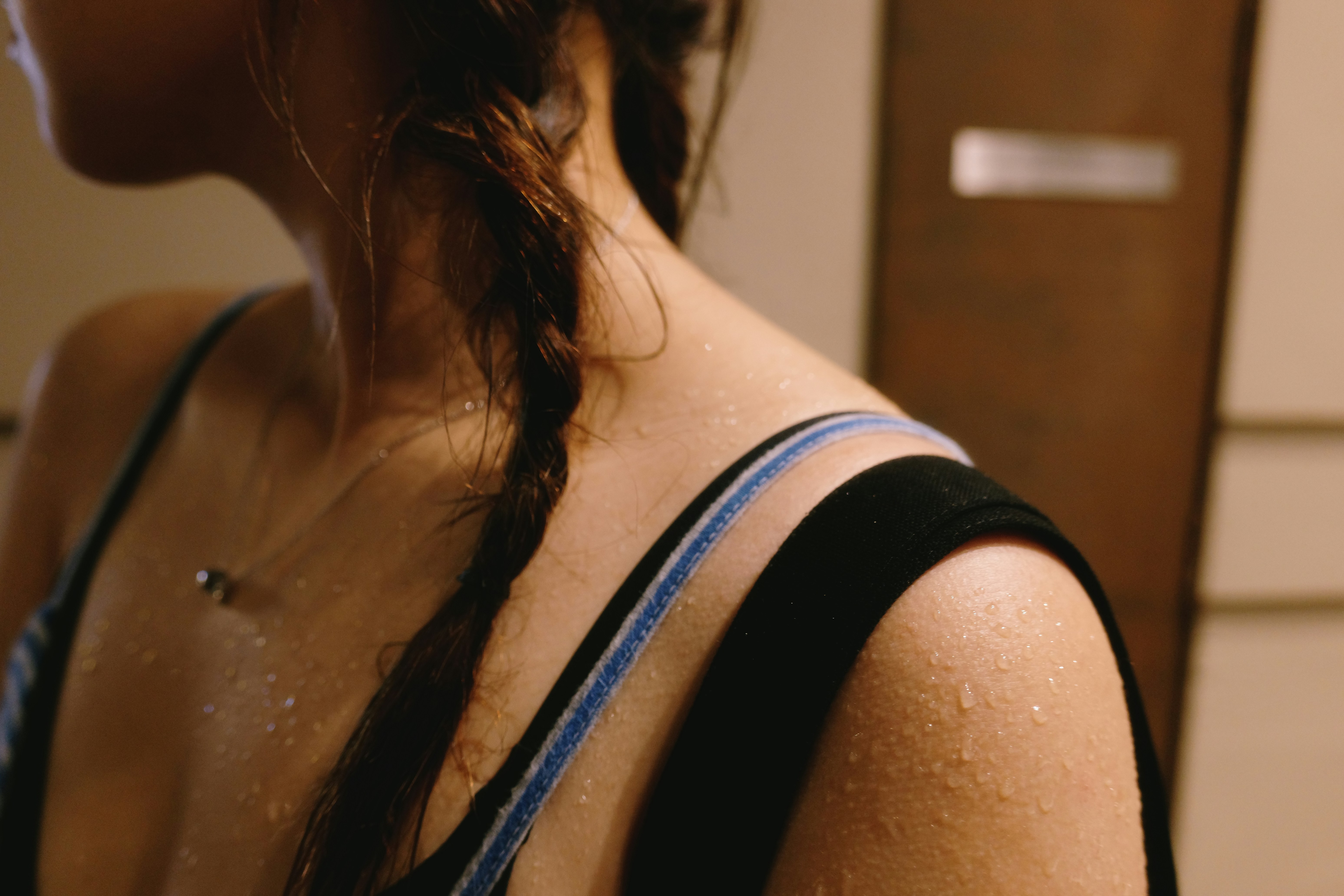 Close-up of a person’s shoulder and braided hair with water droplets glistening on the skin; a cropped portrait emphasizing texture and detail. Photograph type: candid portrait.