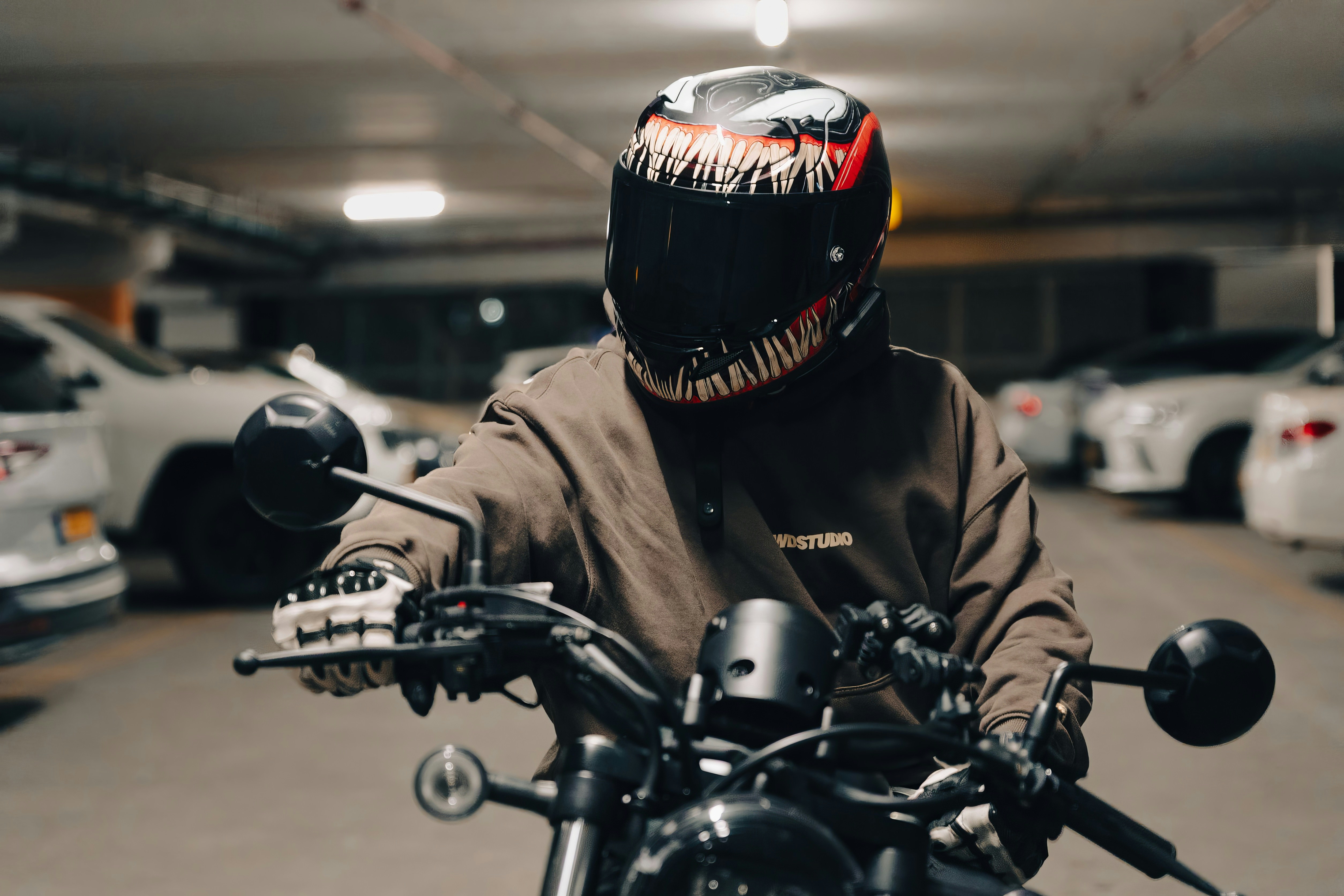 A person wearing a monster-themed helmet on a motorcycle in a parking garage