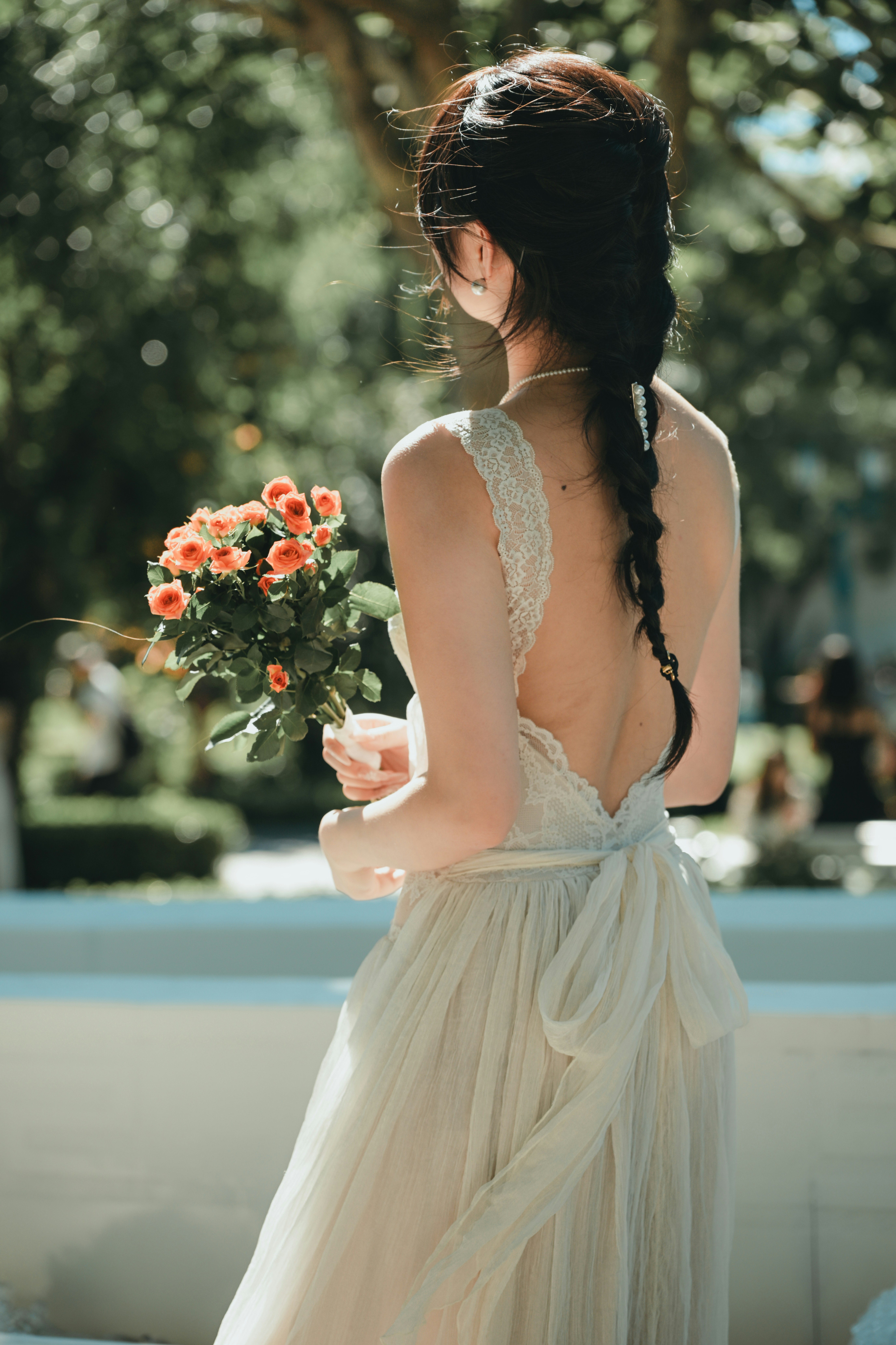 A woman in a lace wedding dress holding orange roses in a garden