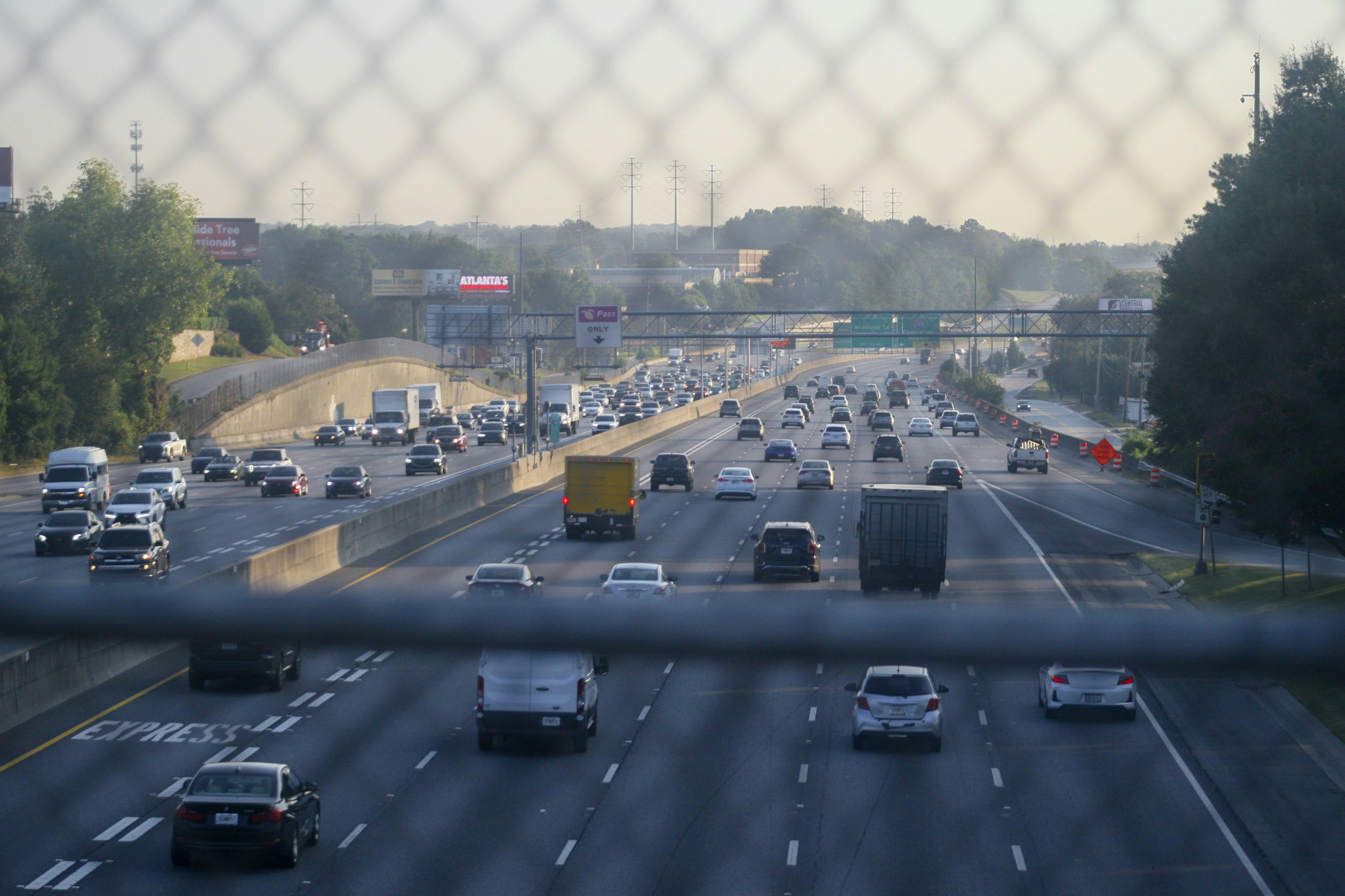 Circulation dense sur une autoroute à plusieurs voies, vue à travers un grillage, un jour de départs en vacances