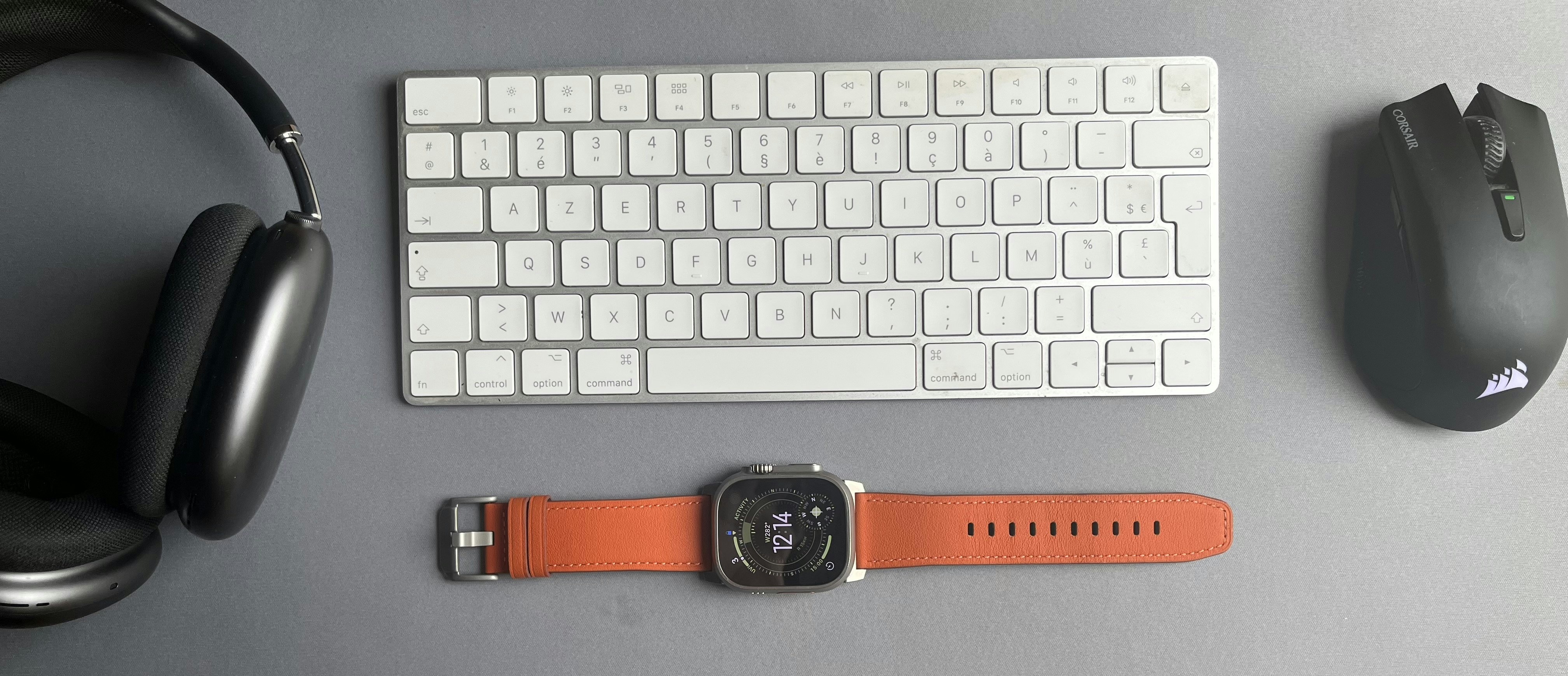 Headphones, a white keyboard, a computer mouse, and a watch with an orange band