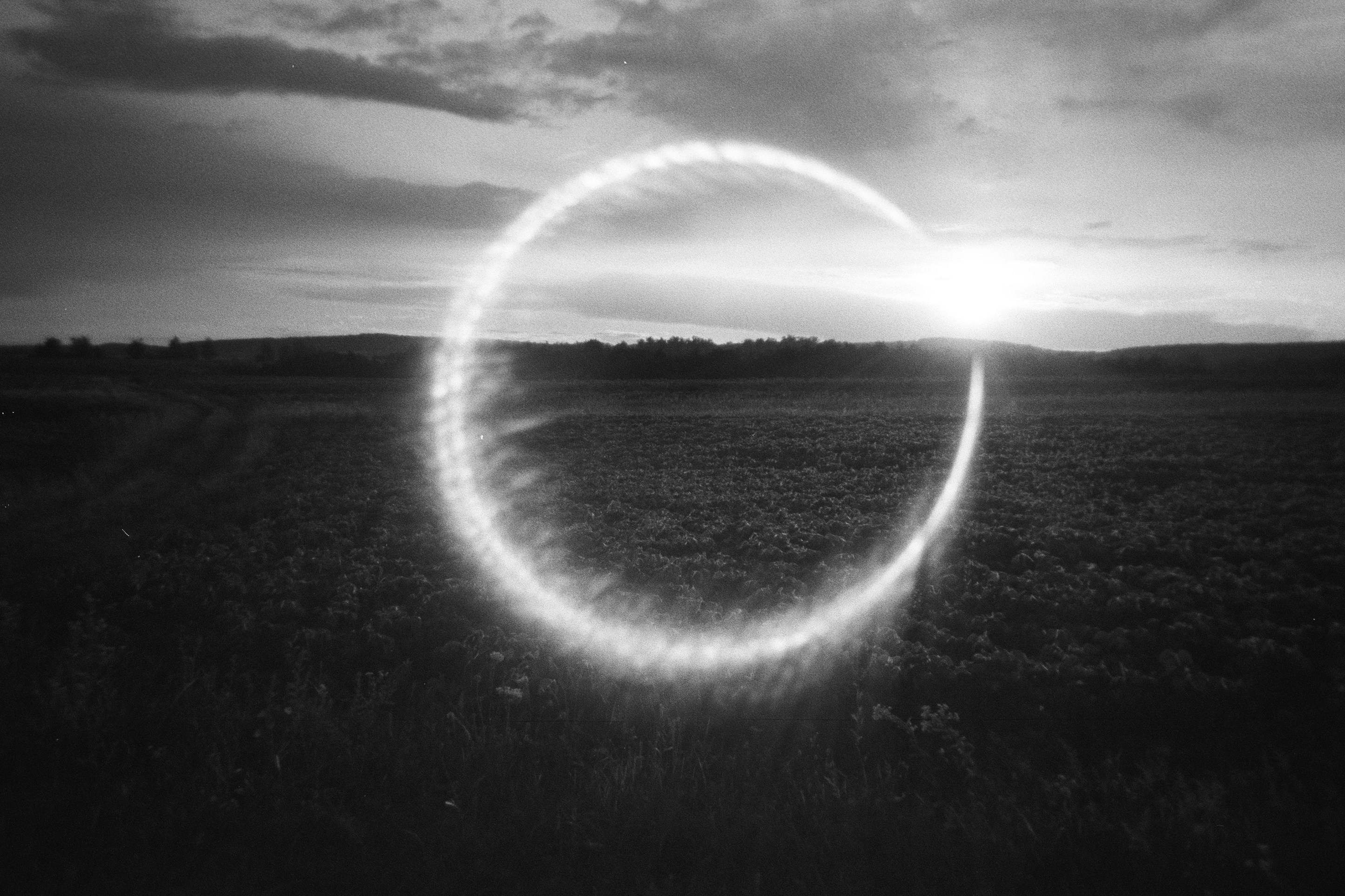 A bright circular lens flare over a dark field under a cloudy sky