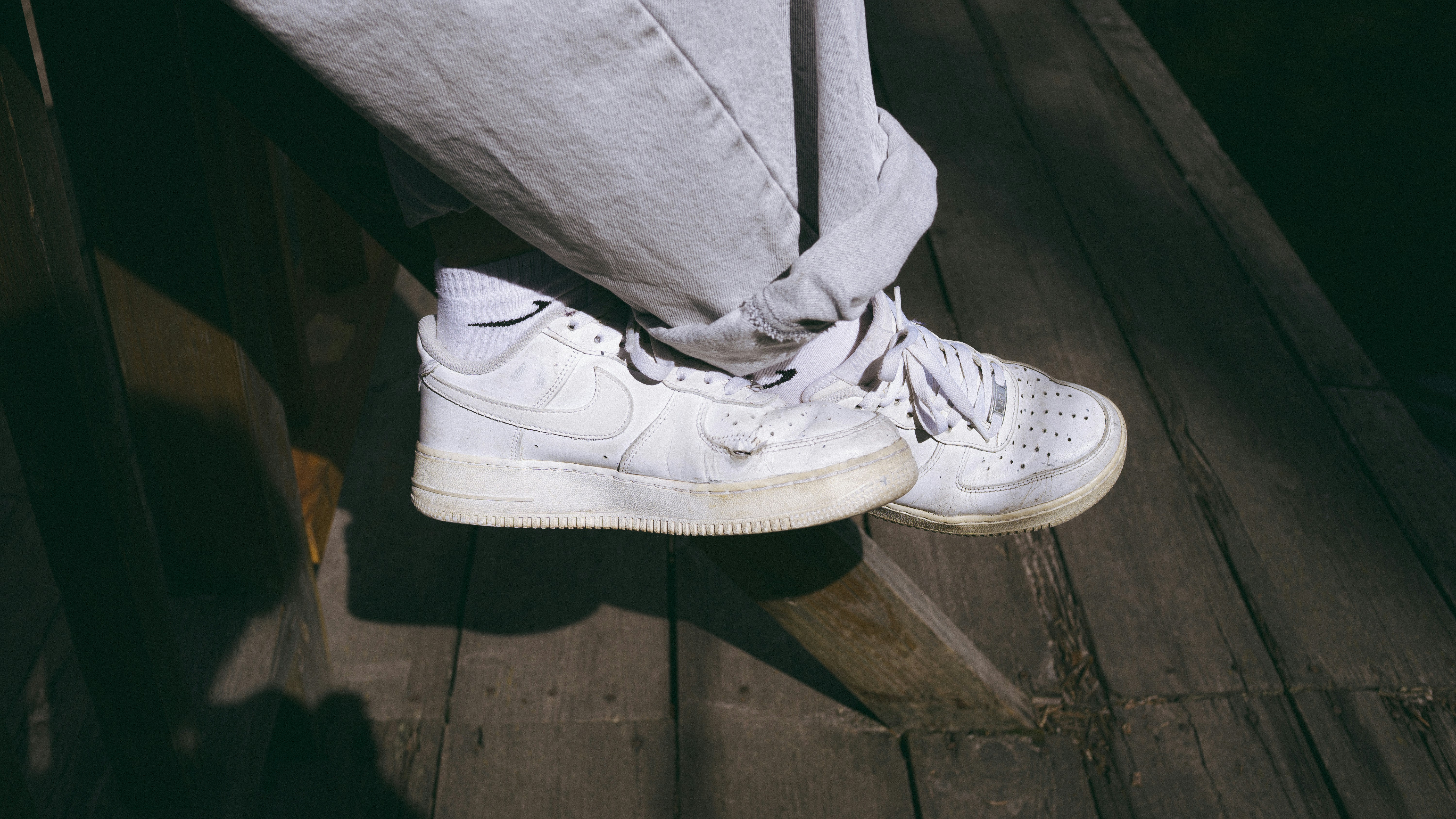 A person wearing white sneakers and white socks on a wooden deck