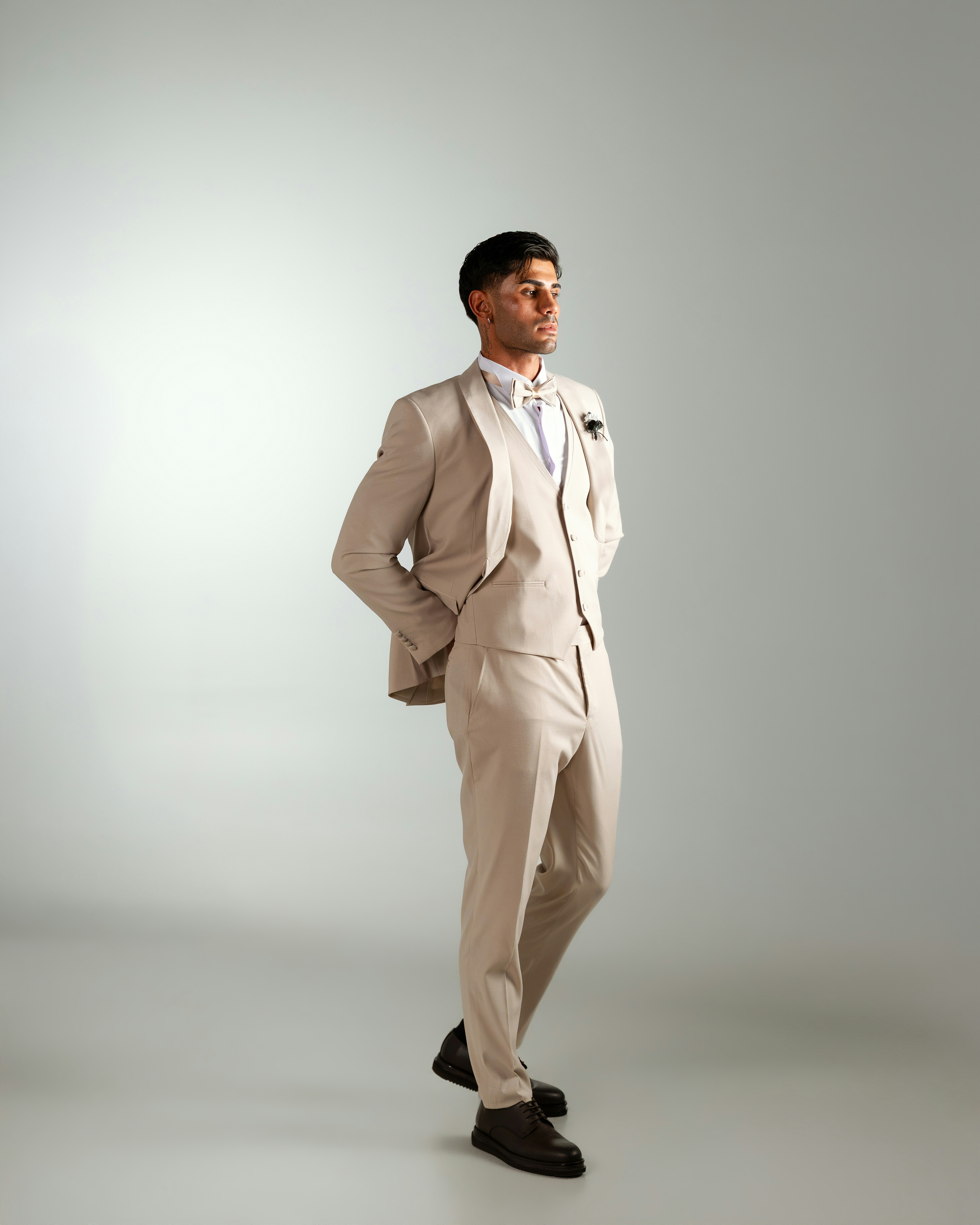 A man in a beige three-piece suit and bow tie on a plain background