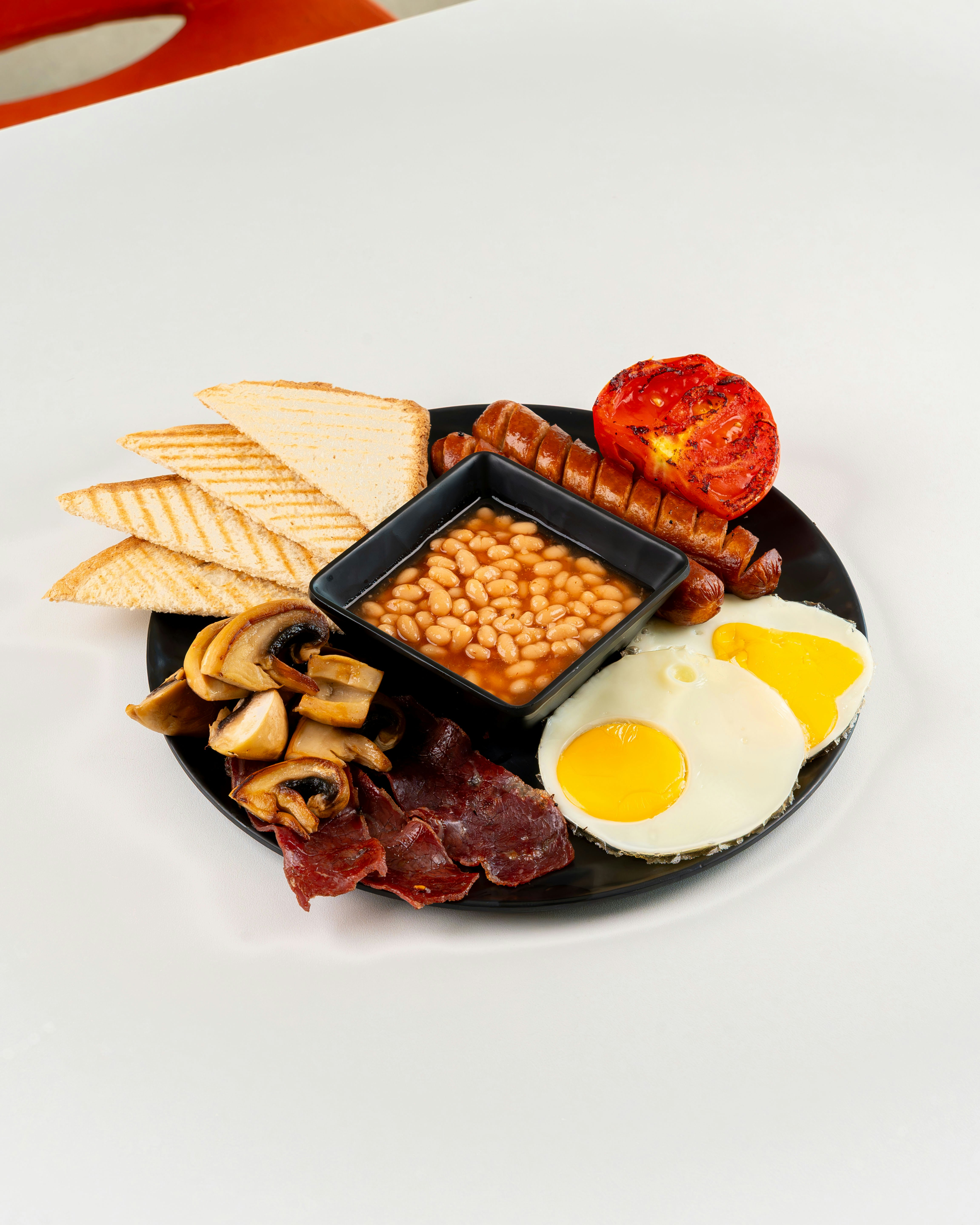 A full English breakfast with eggs, sausage, beans, mushrooms, bacon, tomato, and toast