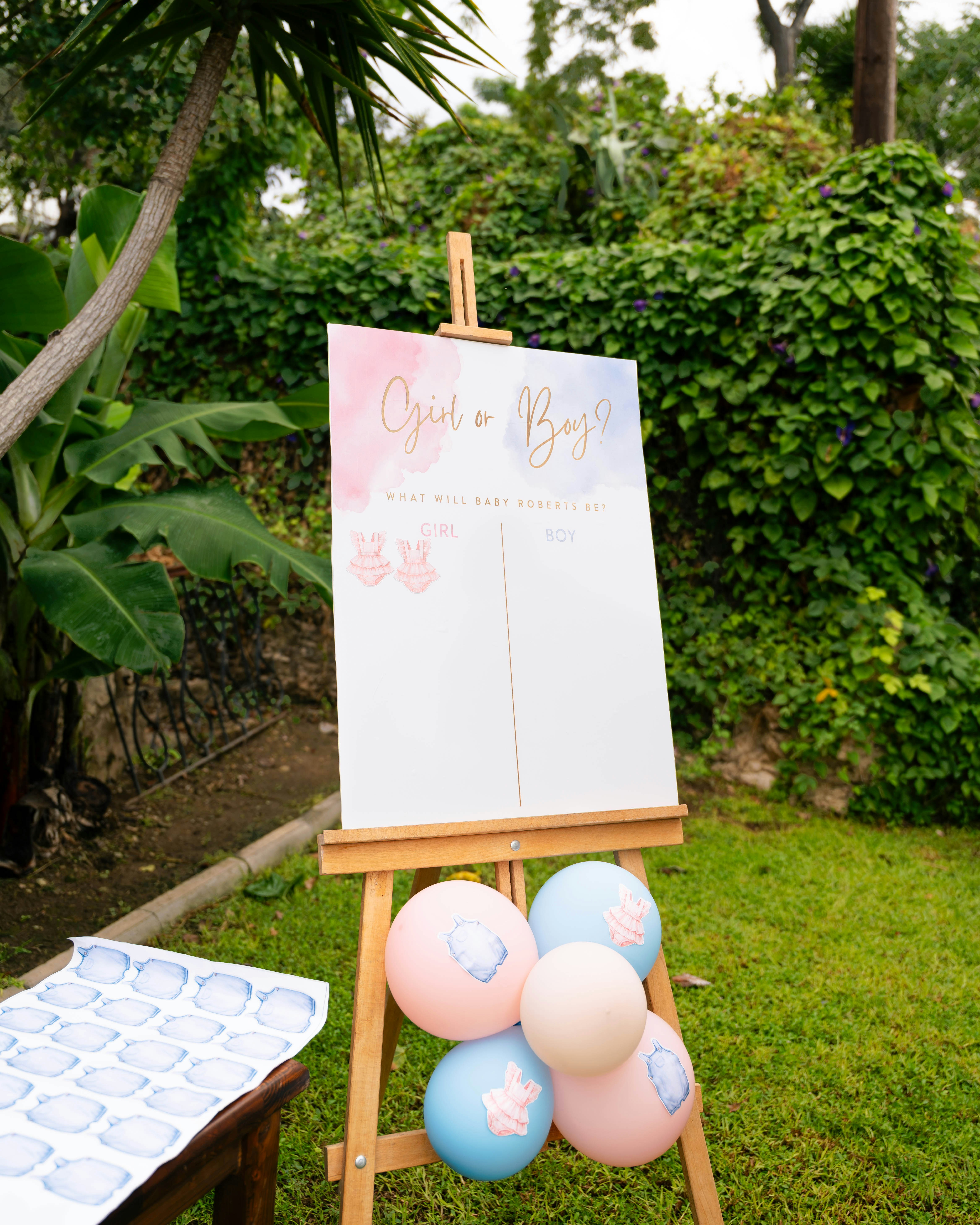 Outdoor garden wedding reception with long white table, pink and white floral arrangements, string lights, and manicured hedges at sunset.