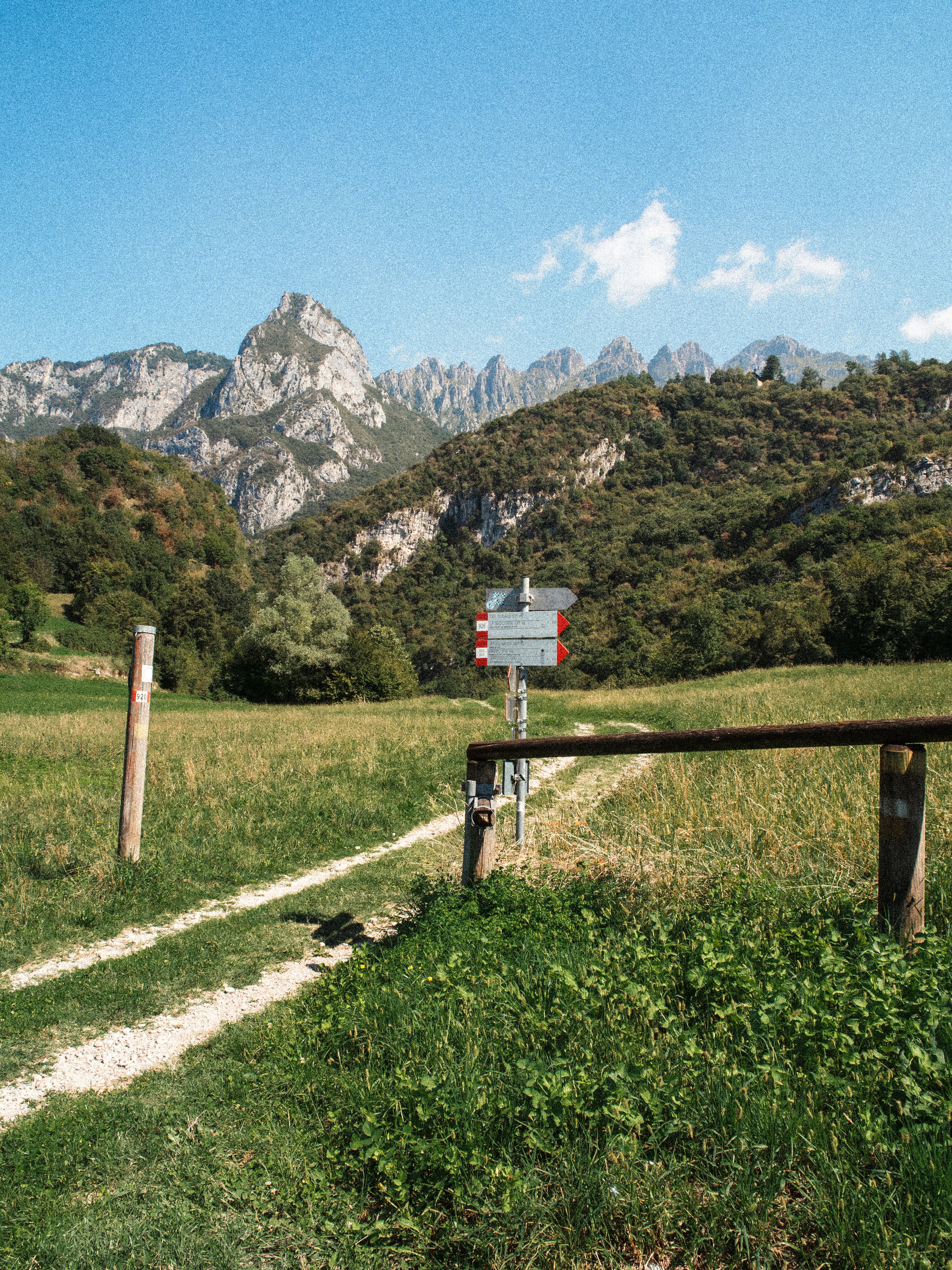 A hiking trail sign in a grassy meadow below jagged mountain peaks