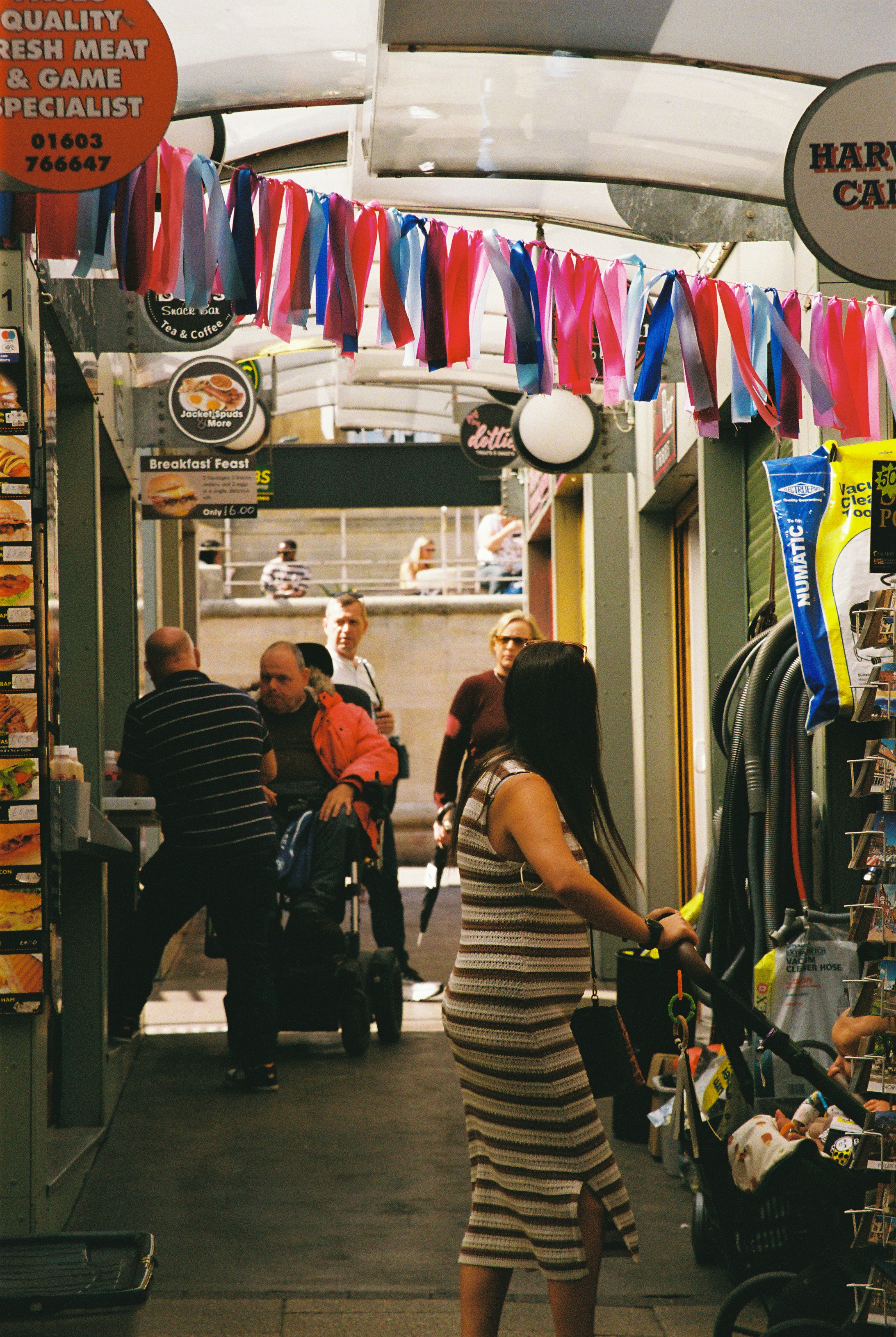 Shoppers in a covered market arcade decorated with colorful pastel bunting