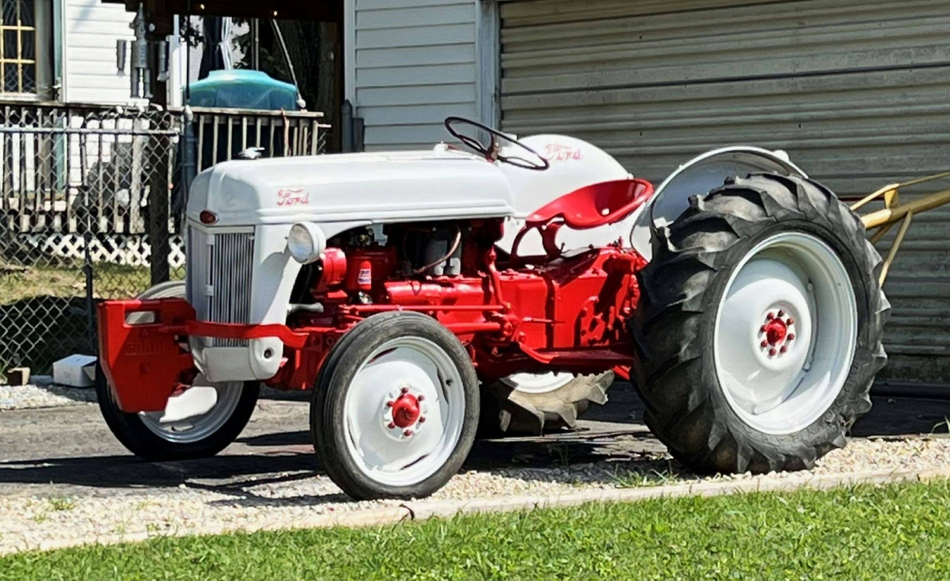 Ein vintage rot-weißer Ford-Traktor, der auf einer Schotterauffahrt geparkt ist