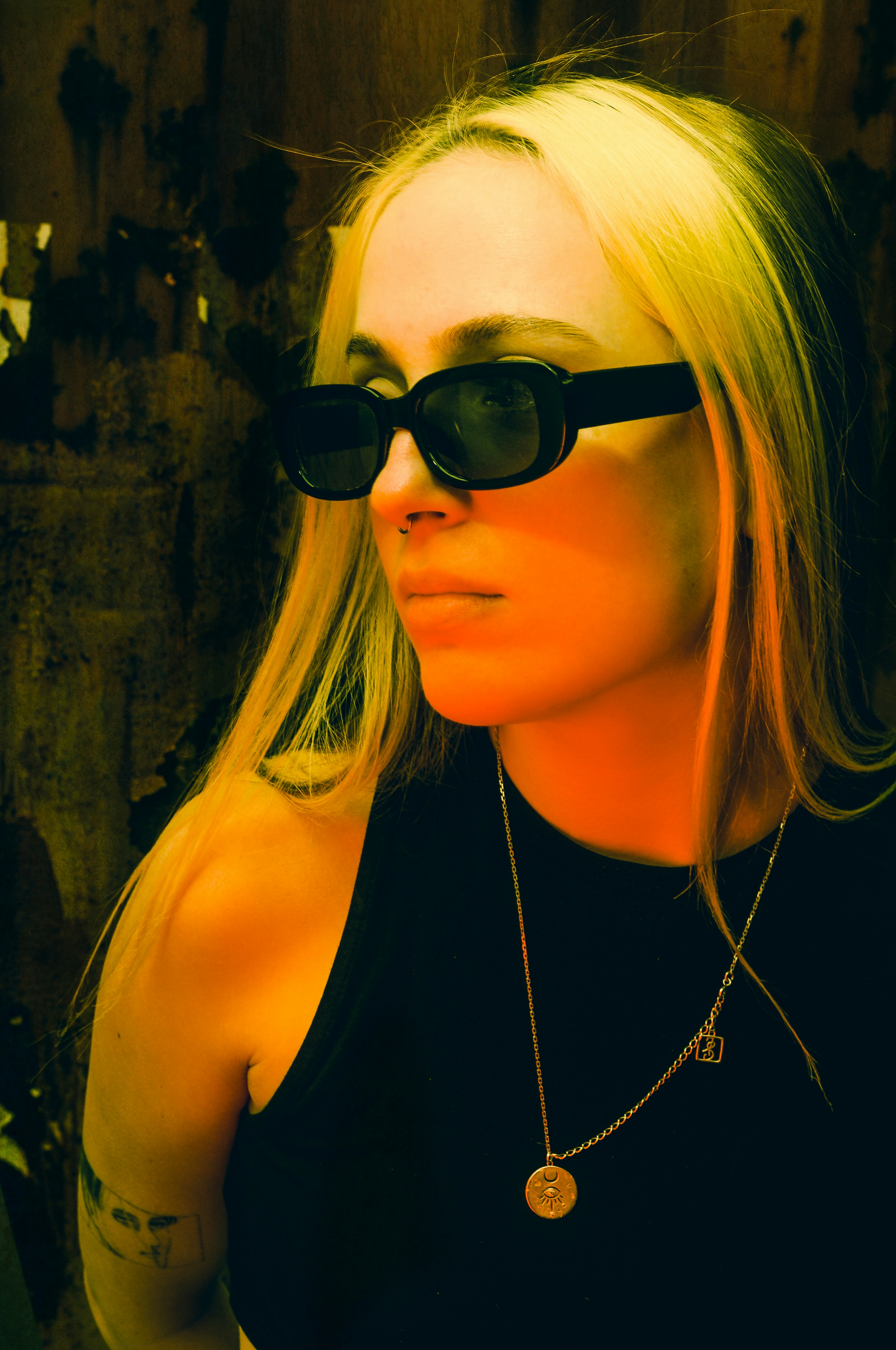 A woman with blonde hair wearing black sunglasses and a gold pendant necklace