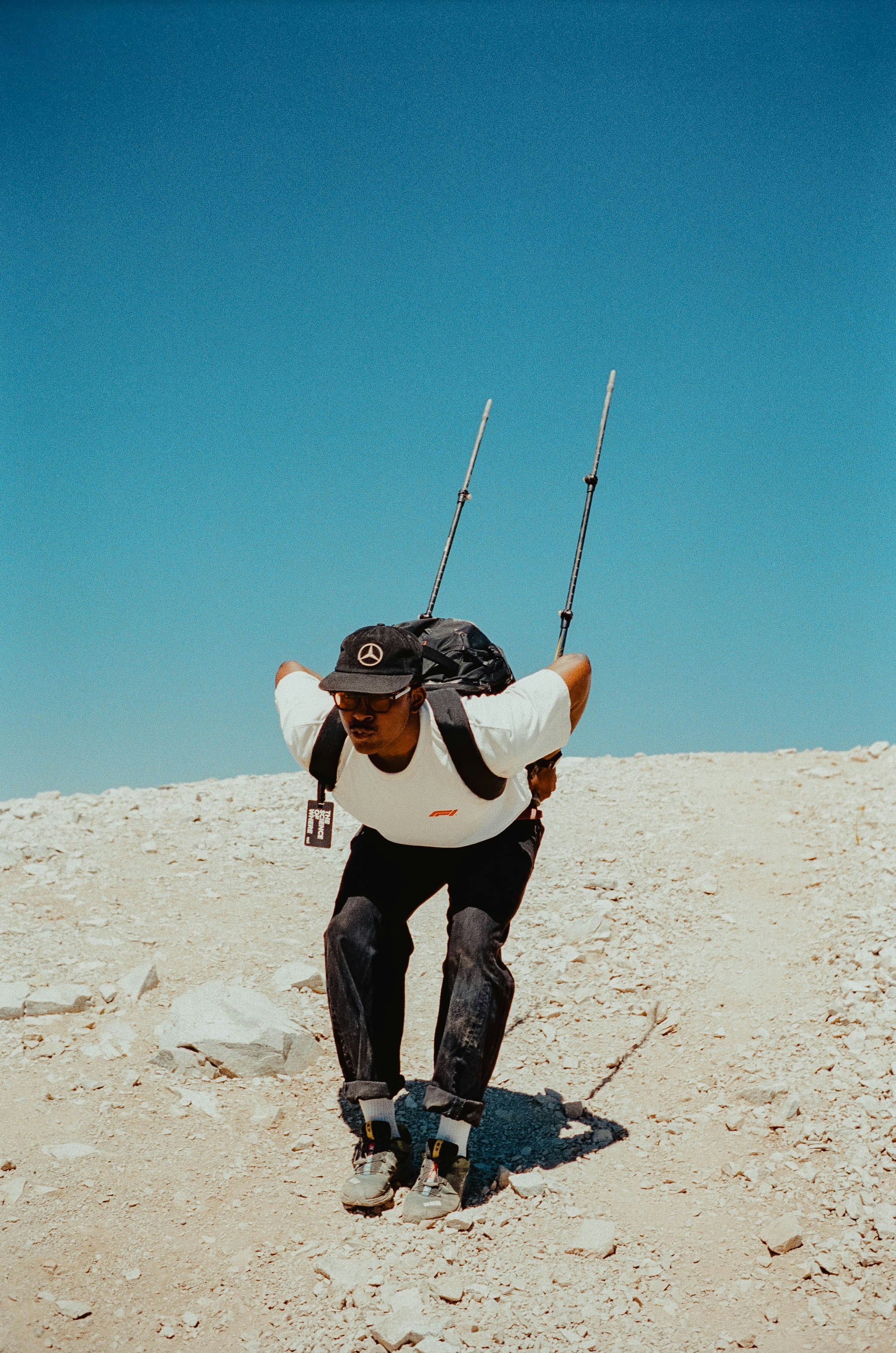 A person in a white t-shirt and cap hiking on a rocky slope