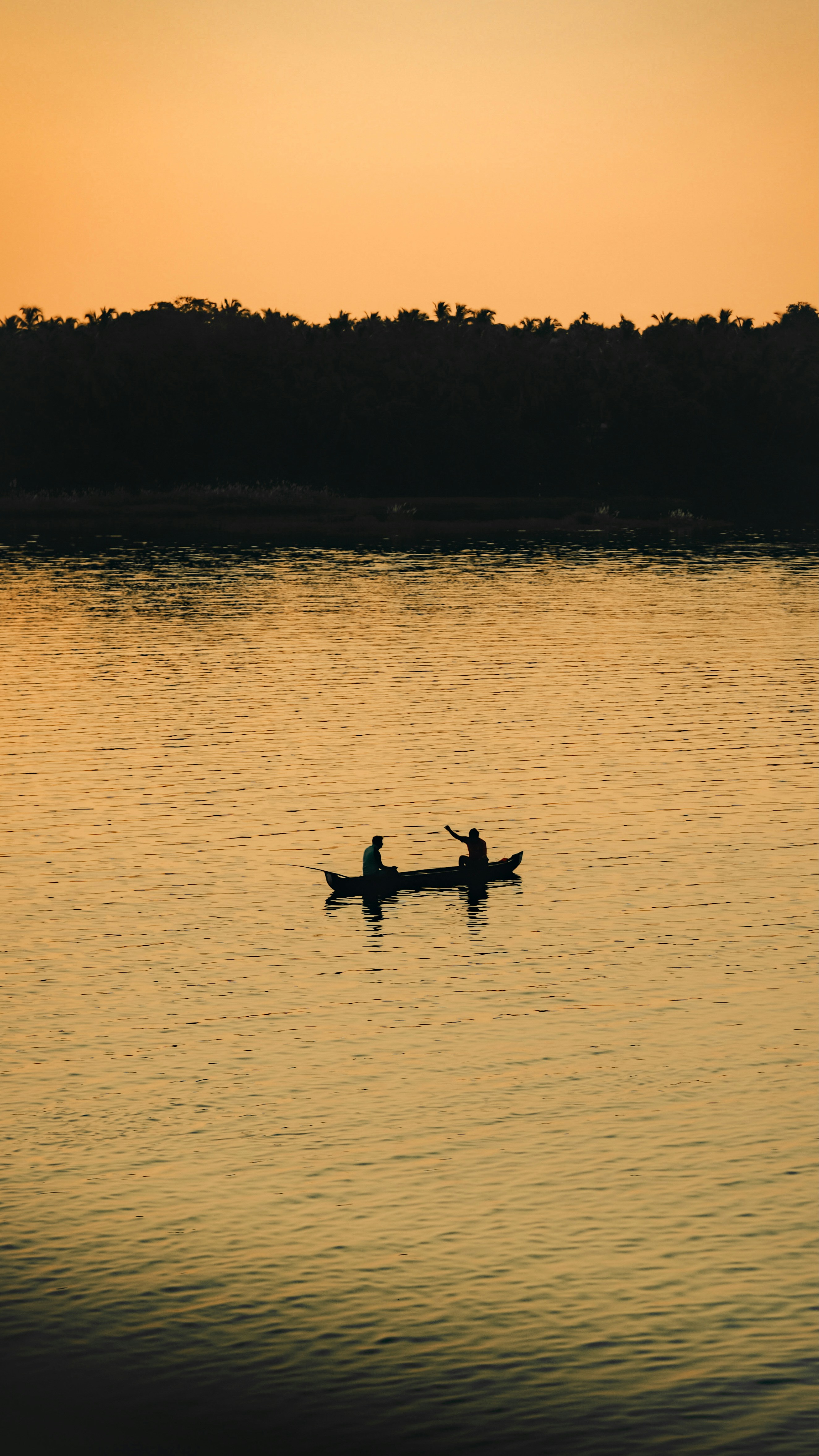 Two people in a small boat on calm water under a warm orange sky