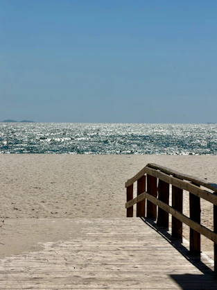 A wooden boardwalk leading to a sandy beach with sparkling ocean water