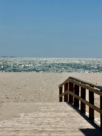 A wooden boardwalk leading to a sandy beach with sparkling ocean water
