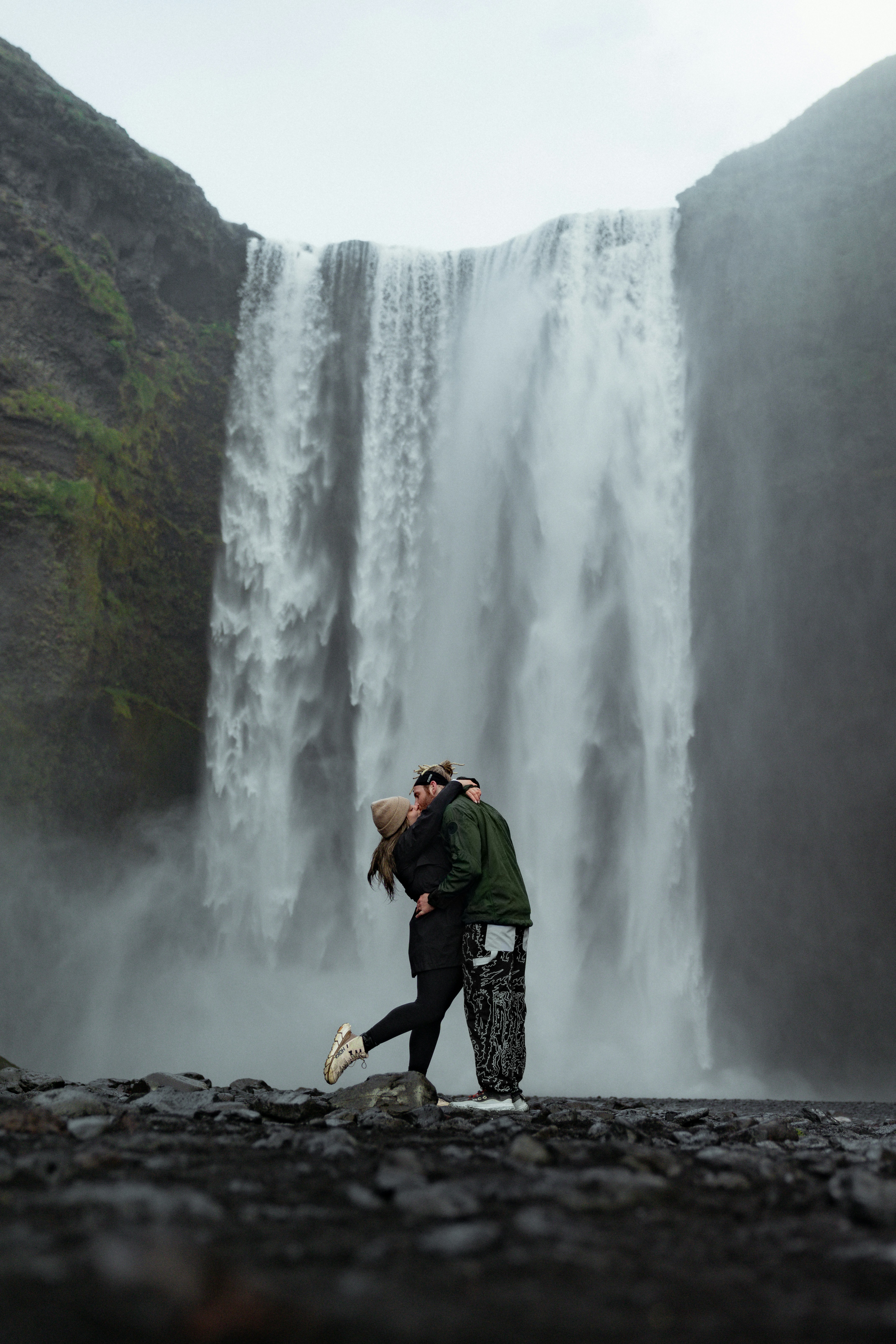 Deux personnes s’embrassant sur un rivage rocheux devant une grande cascade en Islande