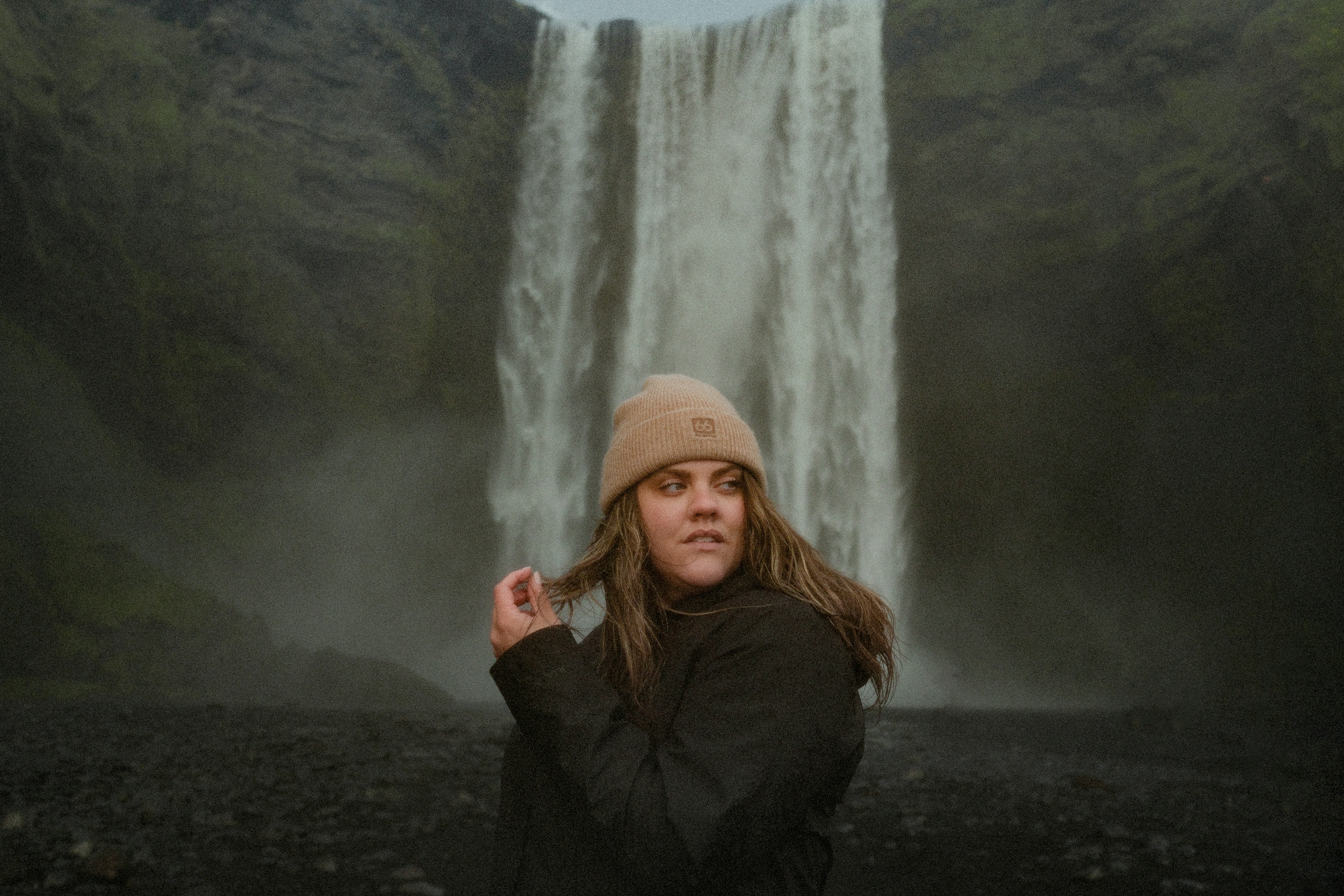 Una donna con un berretto beige e una giacca nera davanti alla cascata di Skogafoss