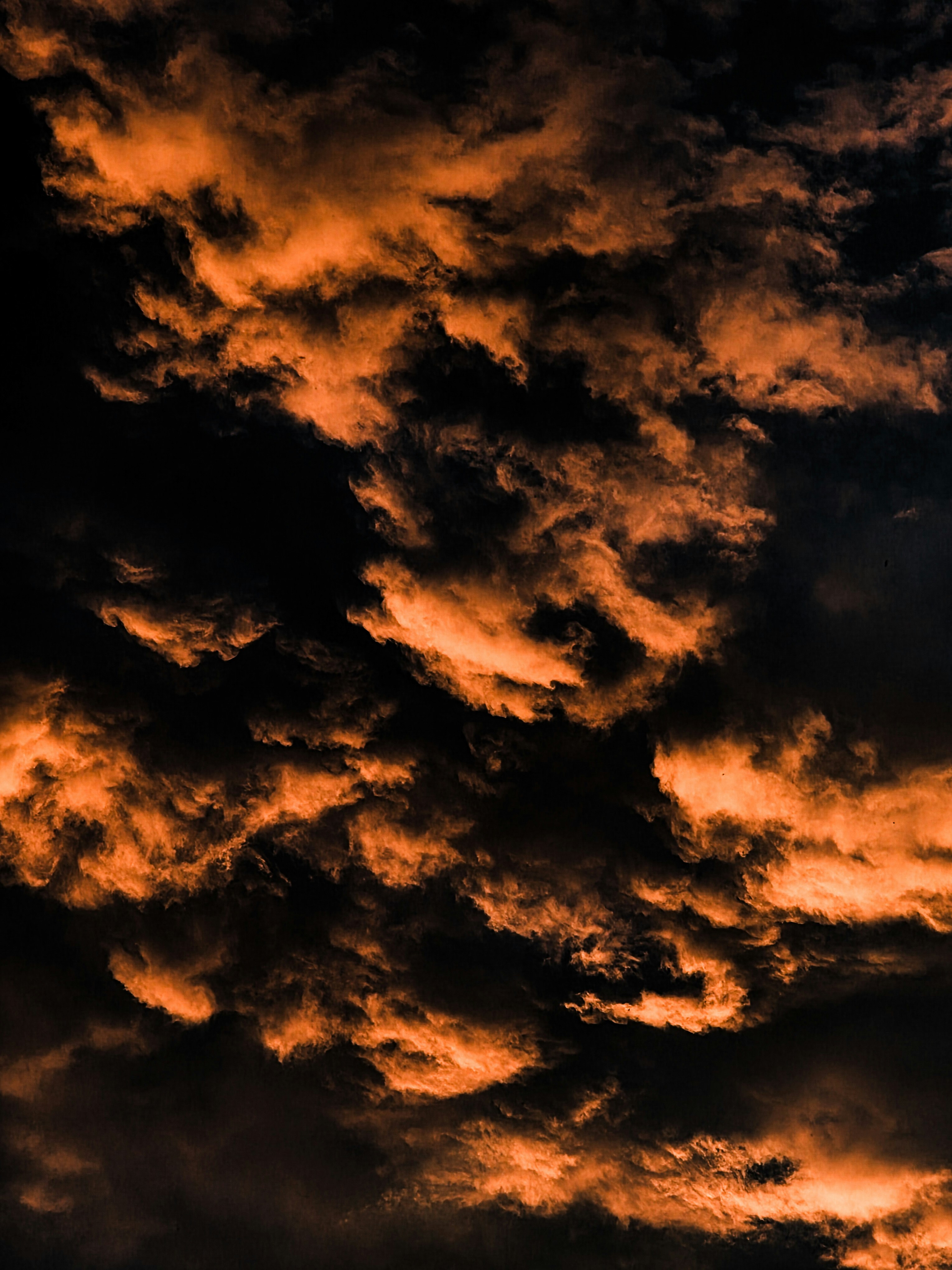 Dark clouds illuminated by warm orange light against a deep black sky