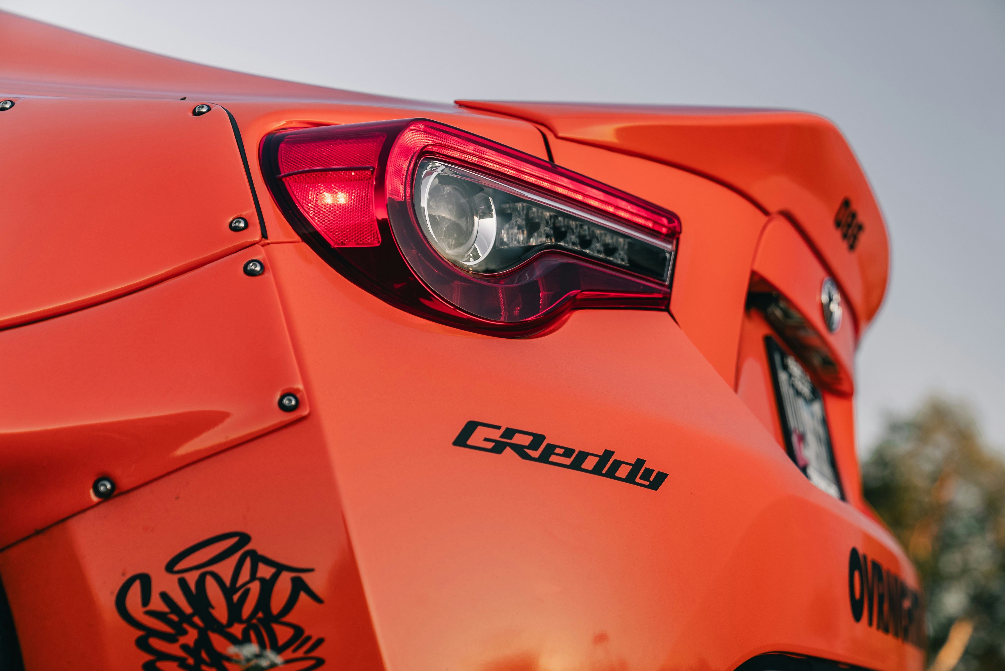 Rear view of a bright orange sports car with a GReddy decal