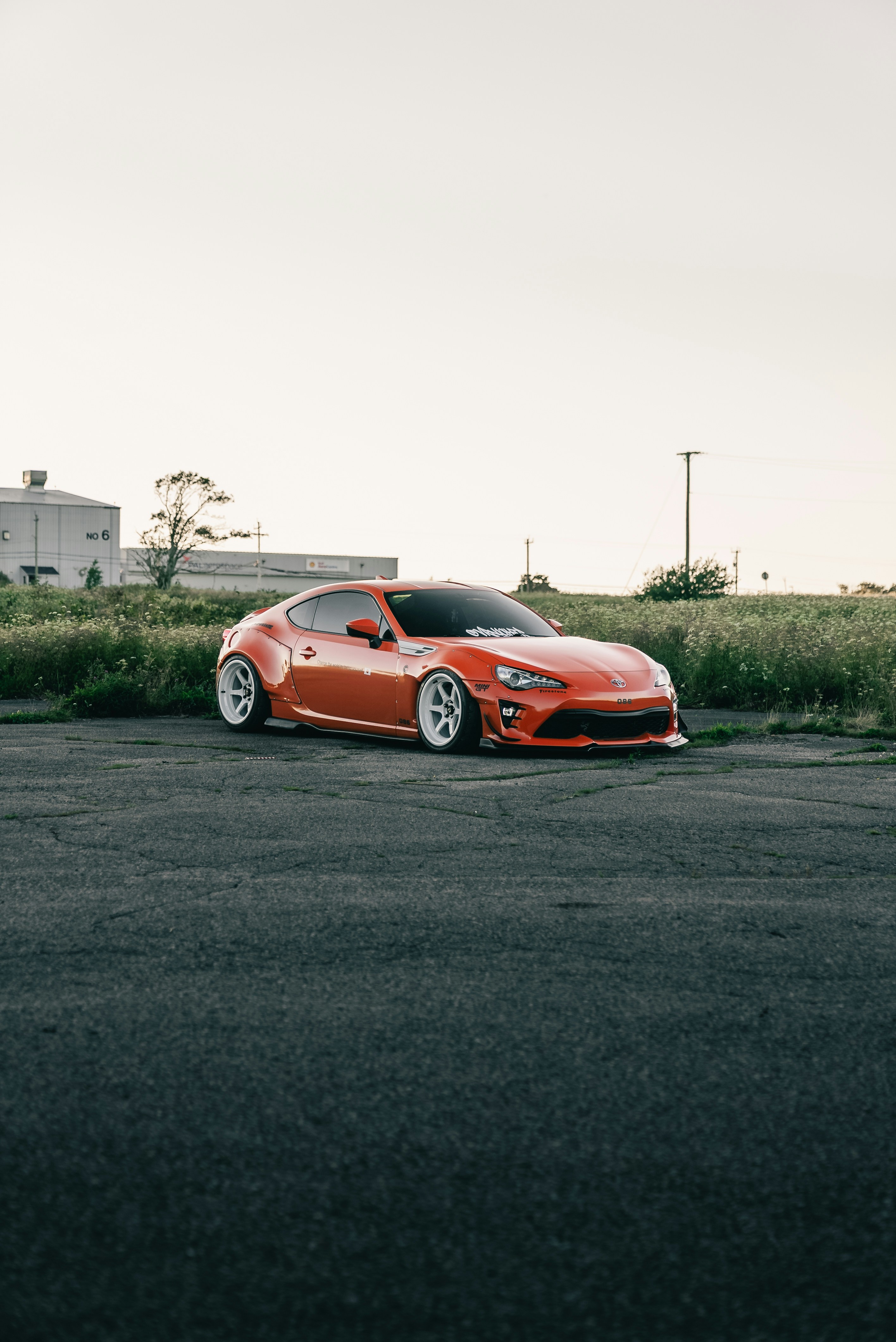 An orange sports car with white wheels parked on an asphalt lot