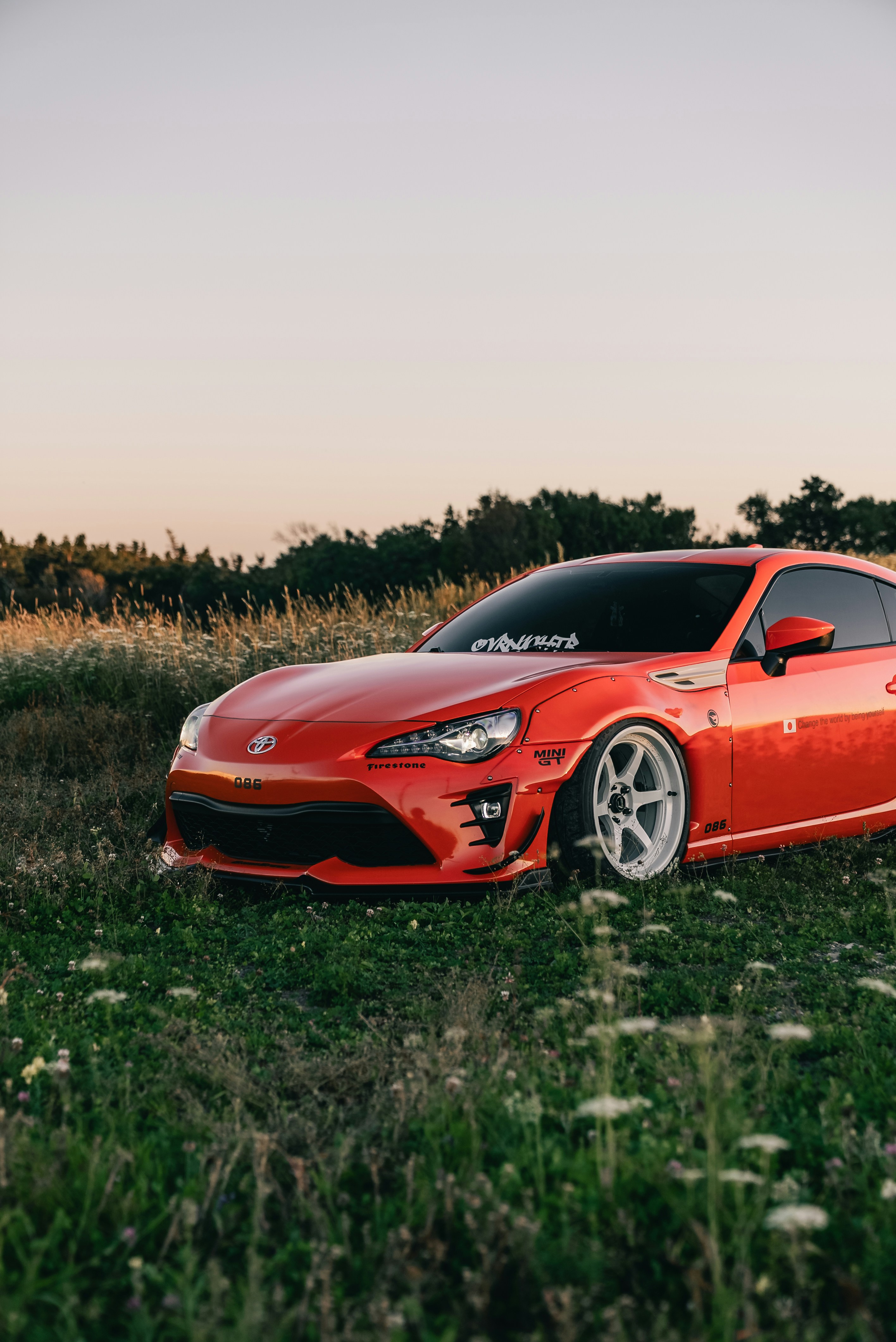 A modified orange sports car parked in a grassy field at golden hour