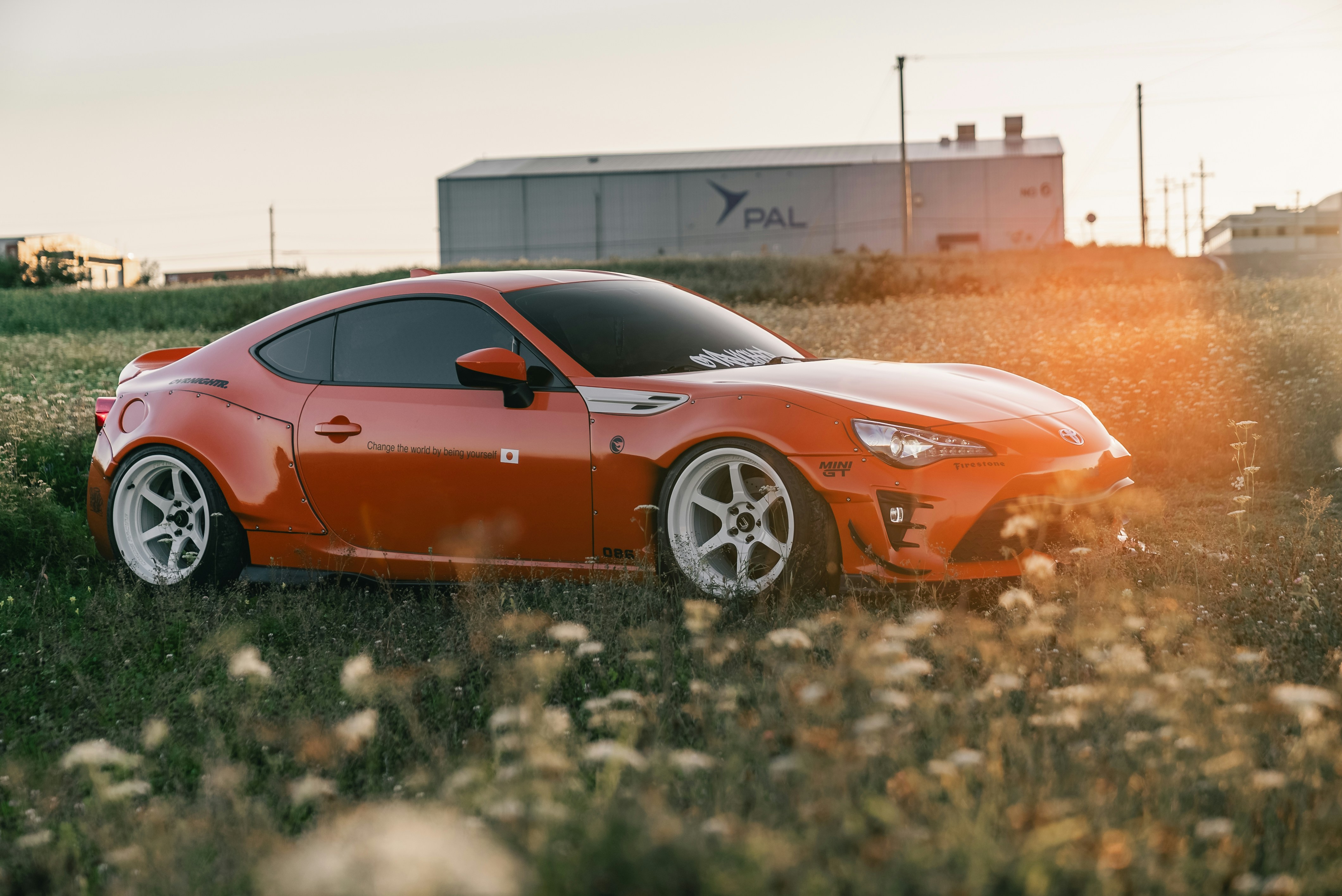 An orange sports car with white wheels parked in a field at golden hour