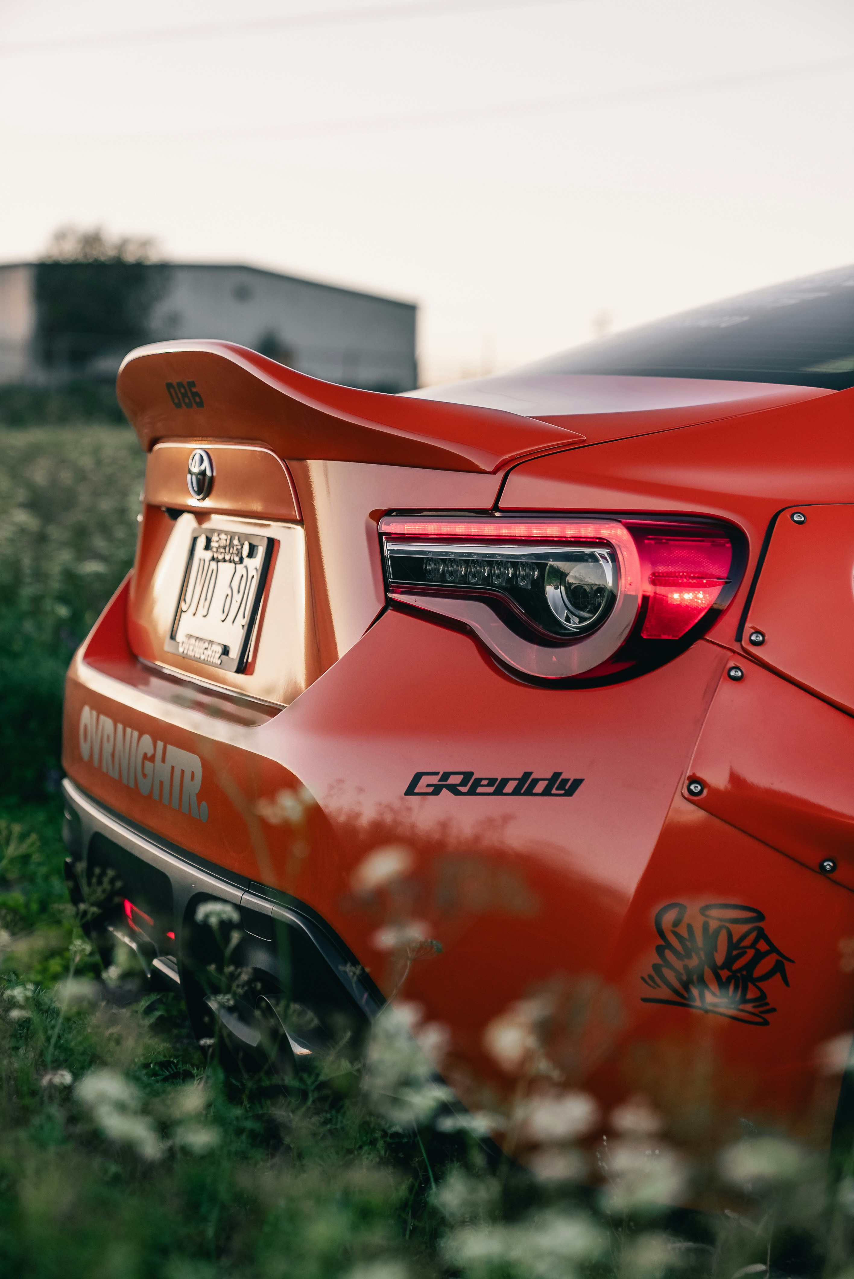Rear view of a modified orange Toyota 86 parked in a grassy field