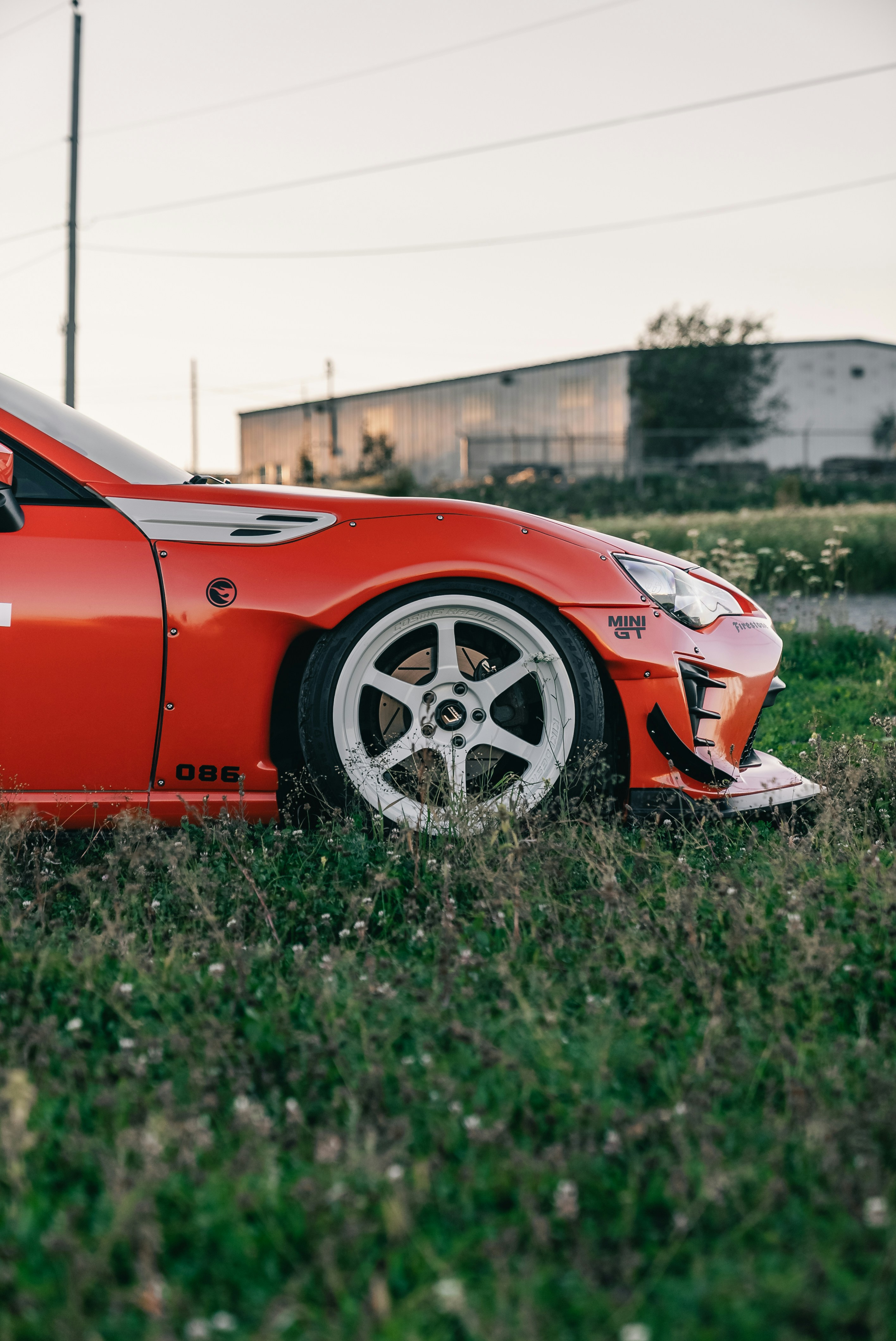 A modified orange sports car with white wheels parked in a grassy field