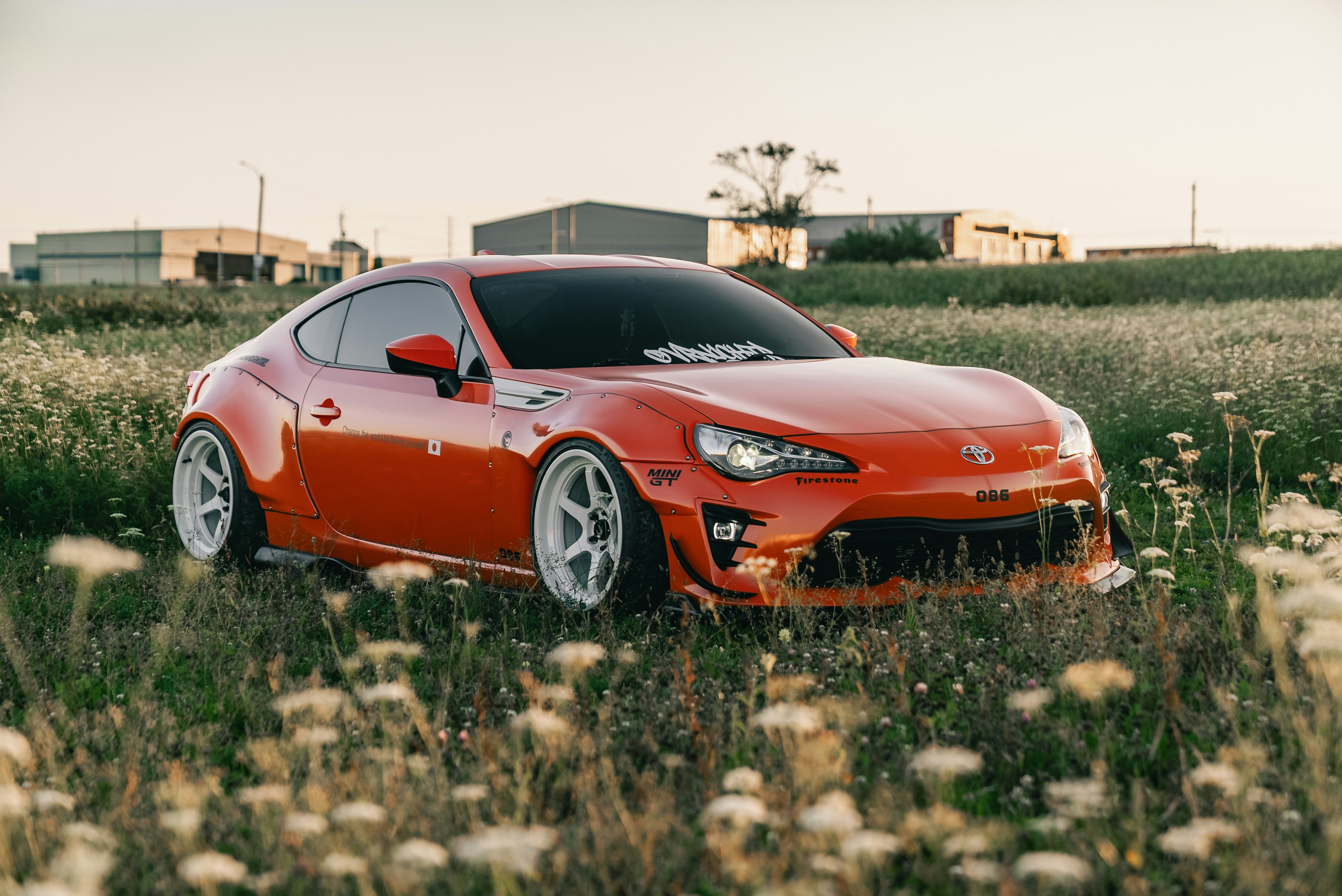 An orange Toyota 86 sports car parked in a field of wildflowers