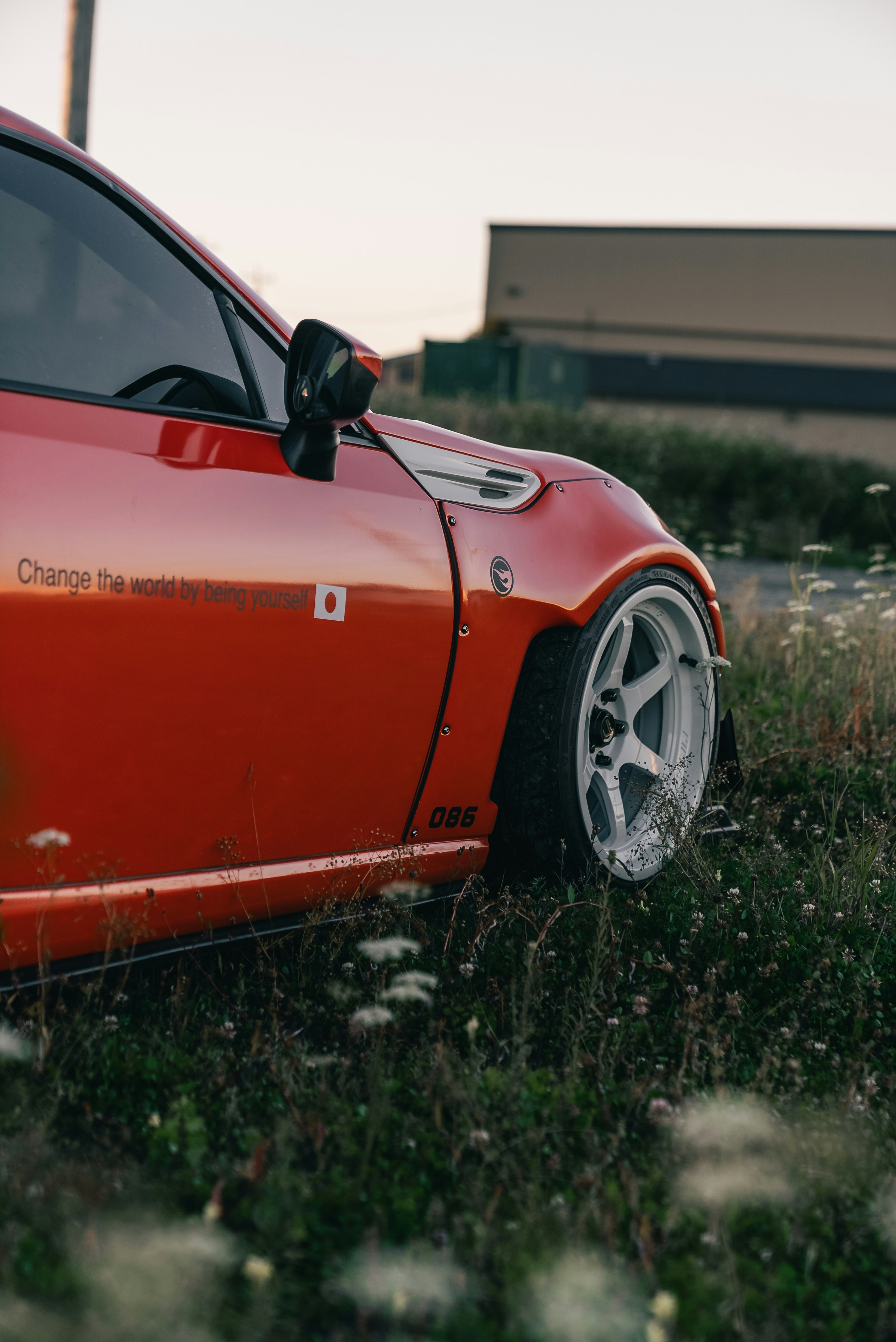 A bright orange sports car with white wheels parked in a grassy field