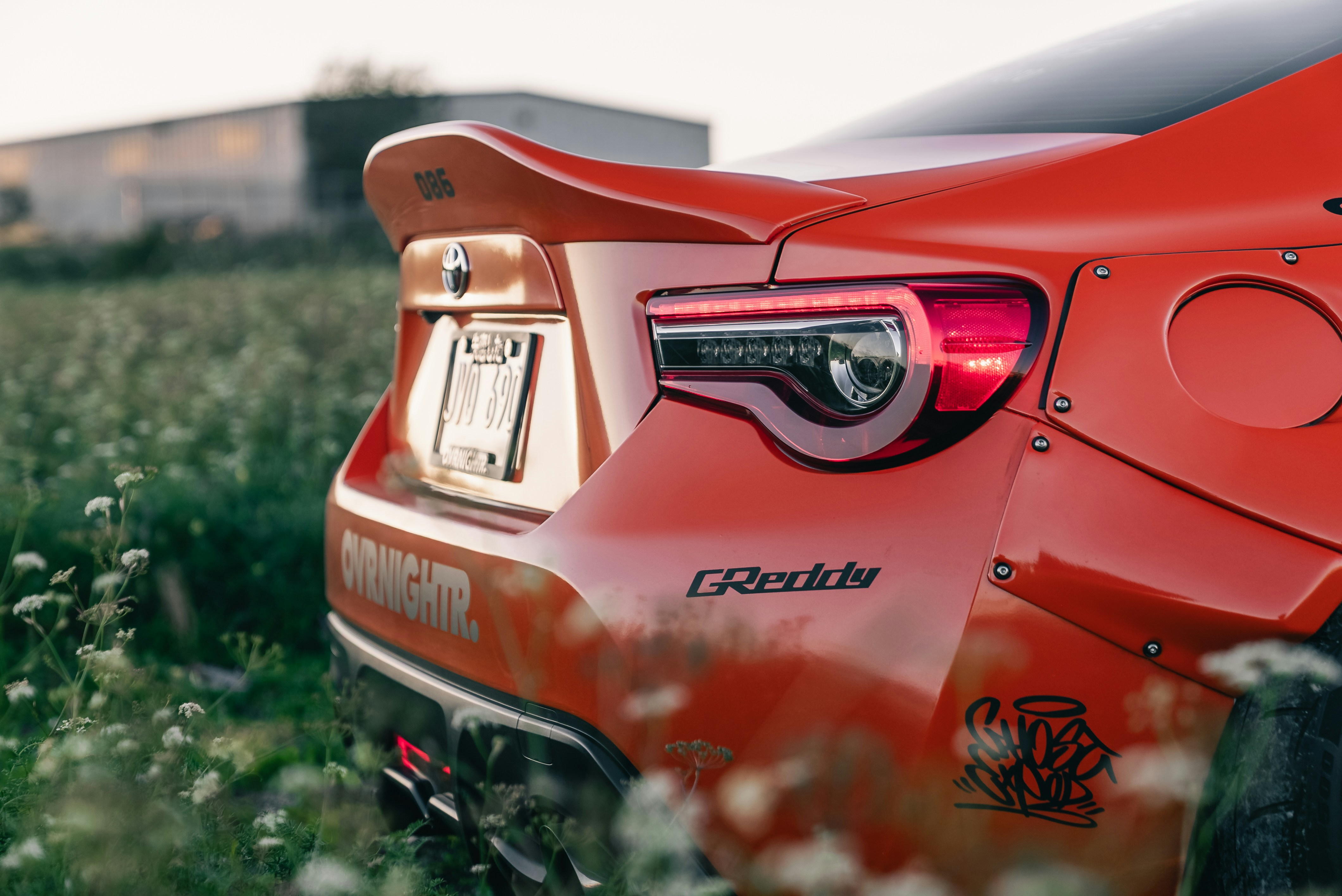 Rear view of a modified orange sports car parked in a grassy field