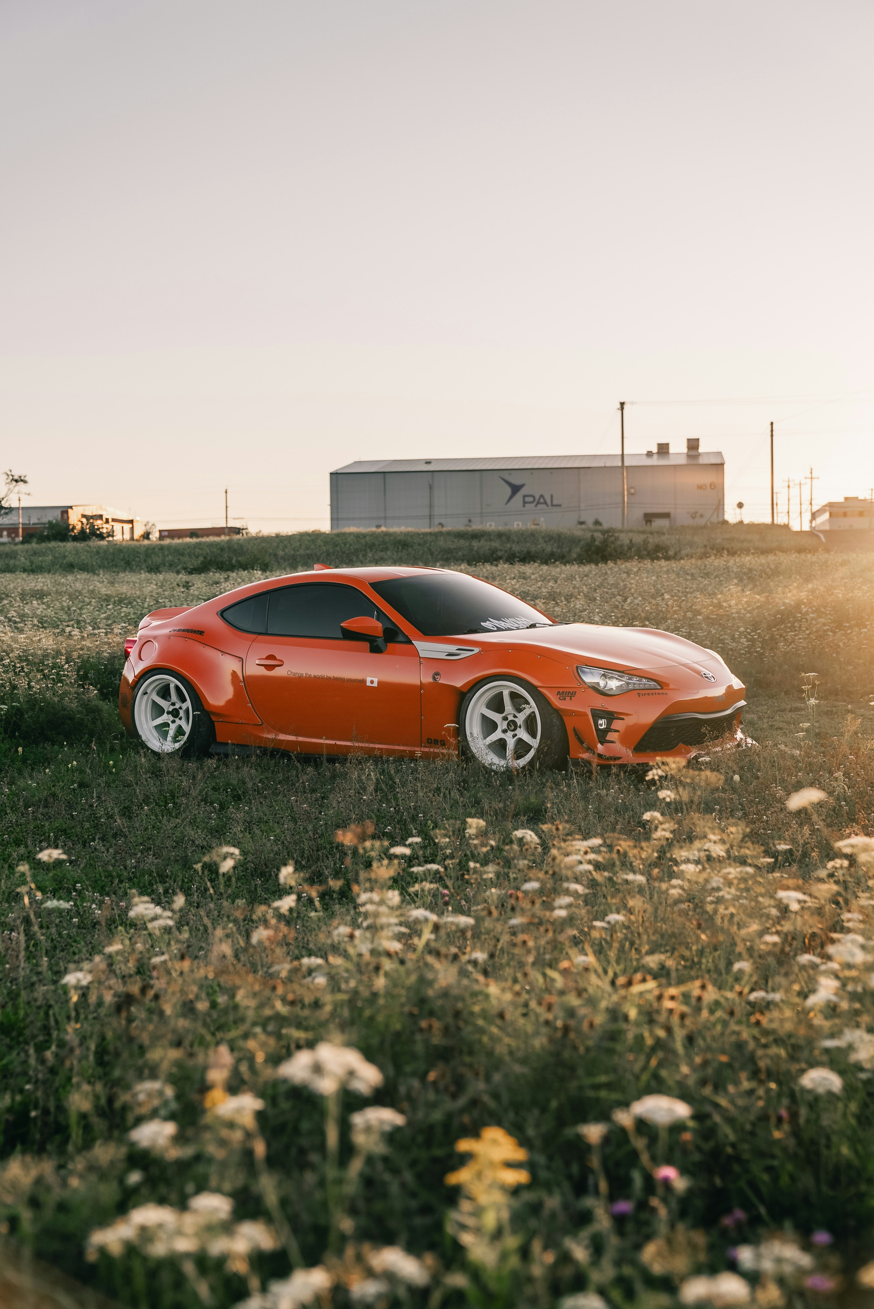 An orange sports car with white wheels parked in a field of wildflowers