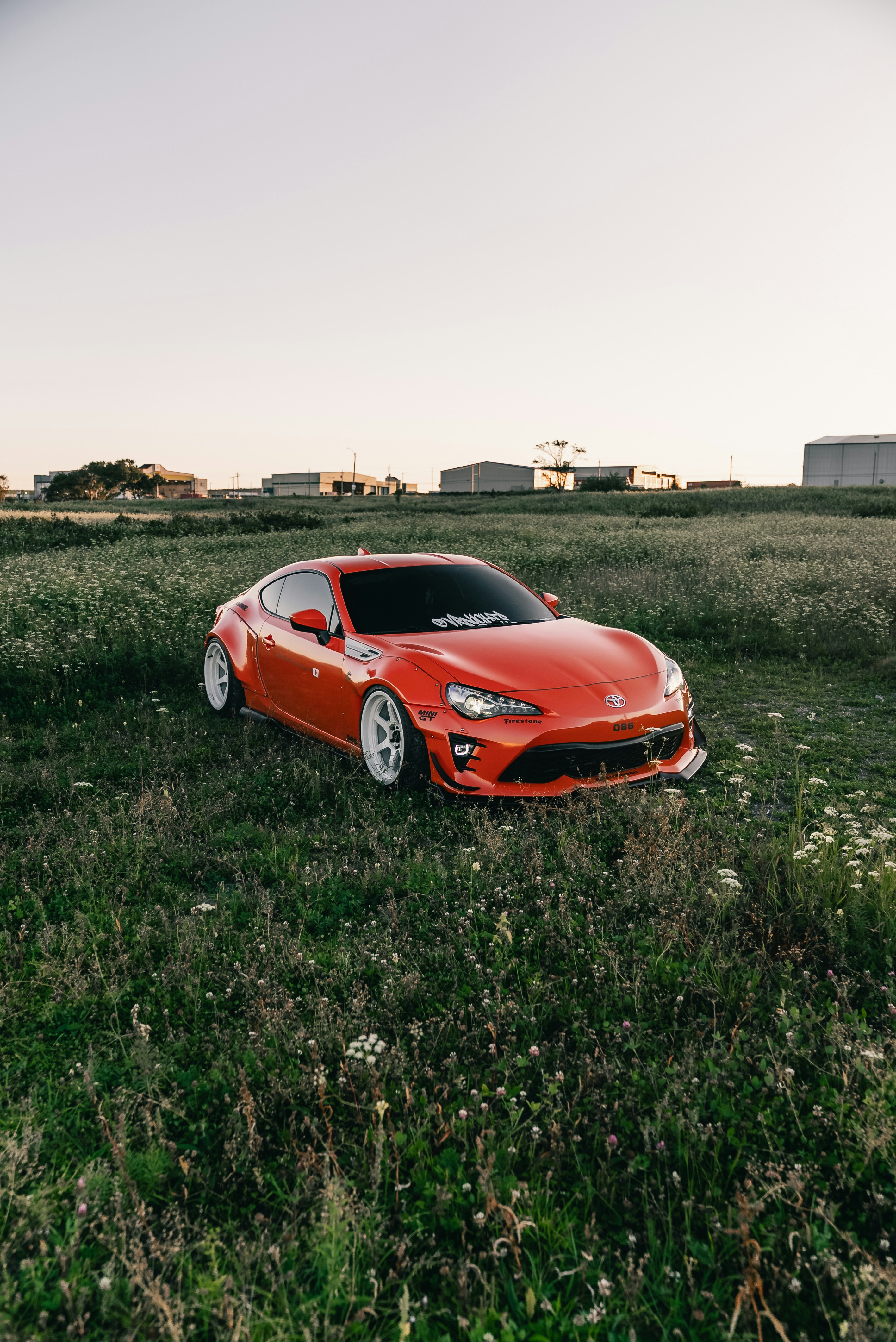 An orange Toyota 86 sports car parked in a grassy field at golden hour