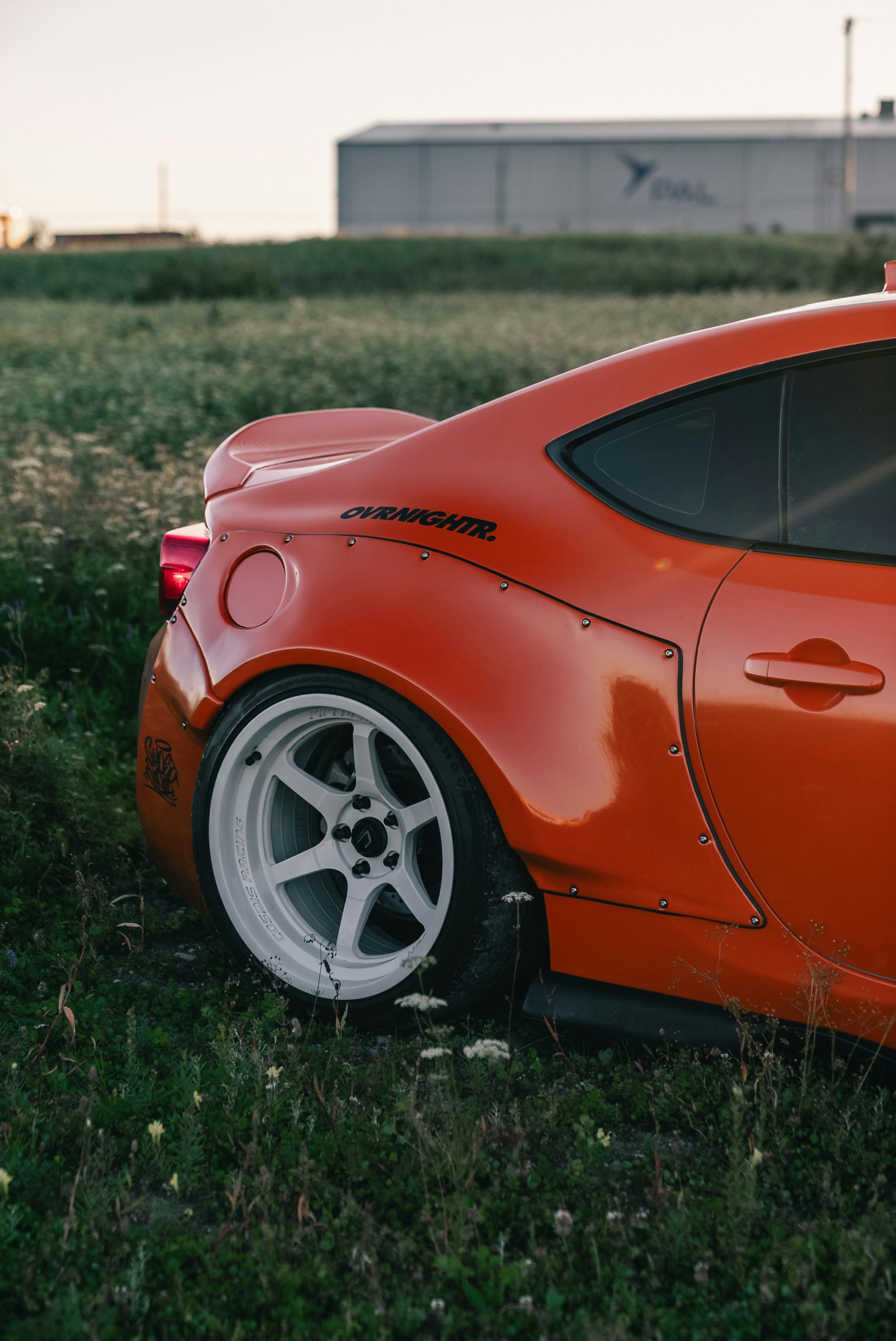 Rear quarter view of an orange sports car with wide fenders in a field