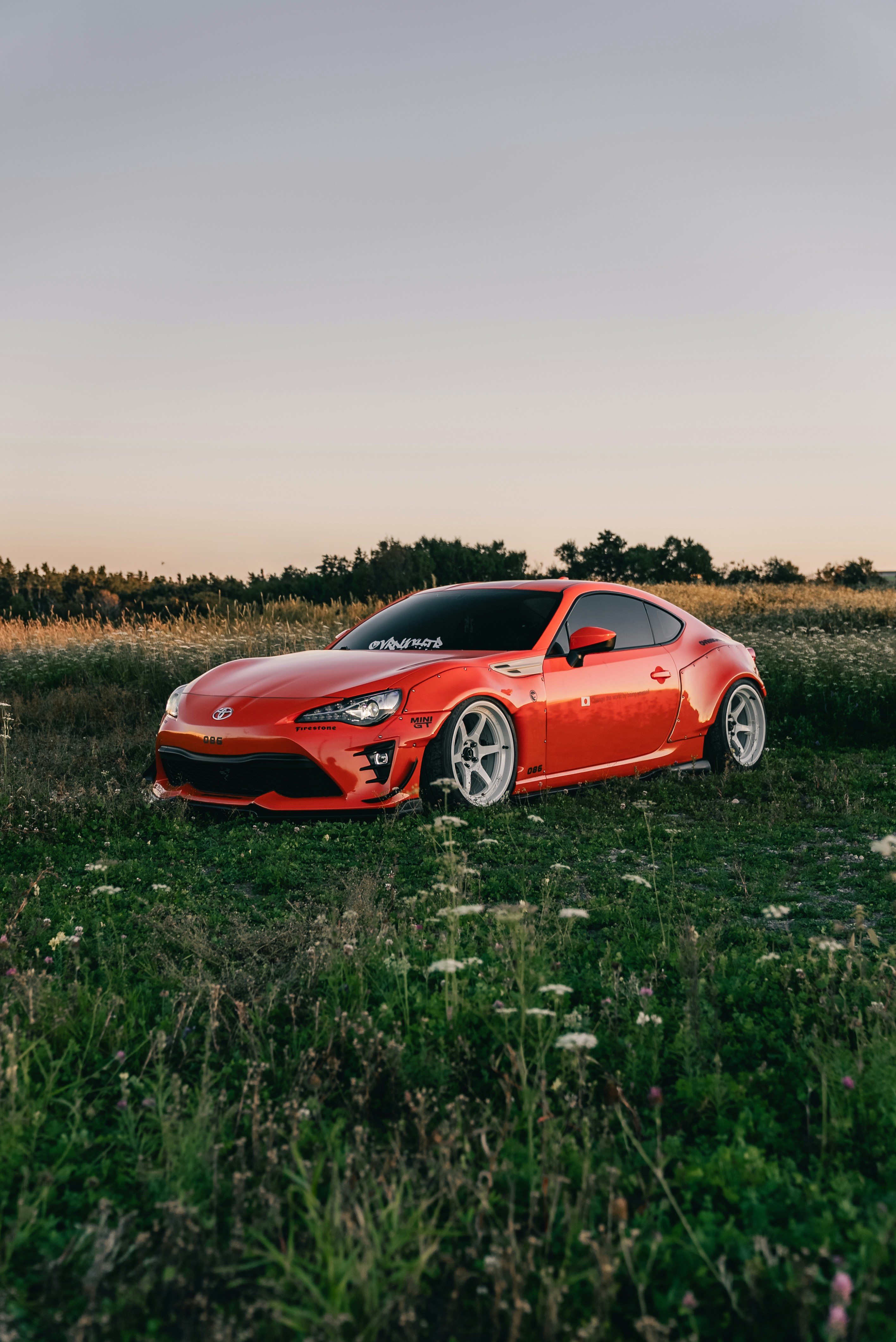 A modified orange sports car parked in a grassy field during golden hour