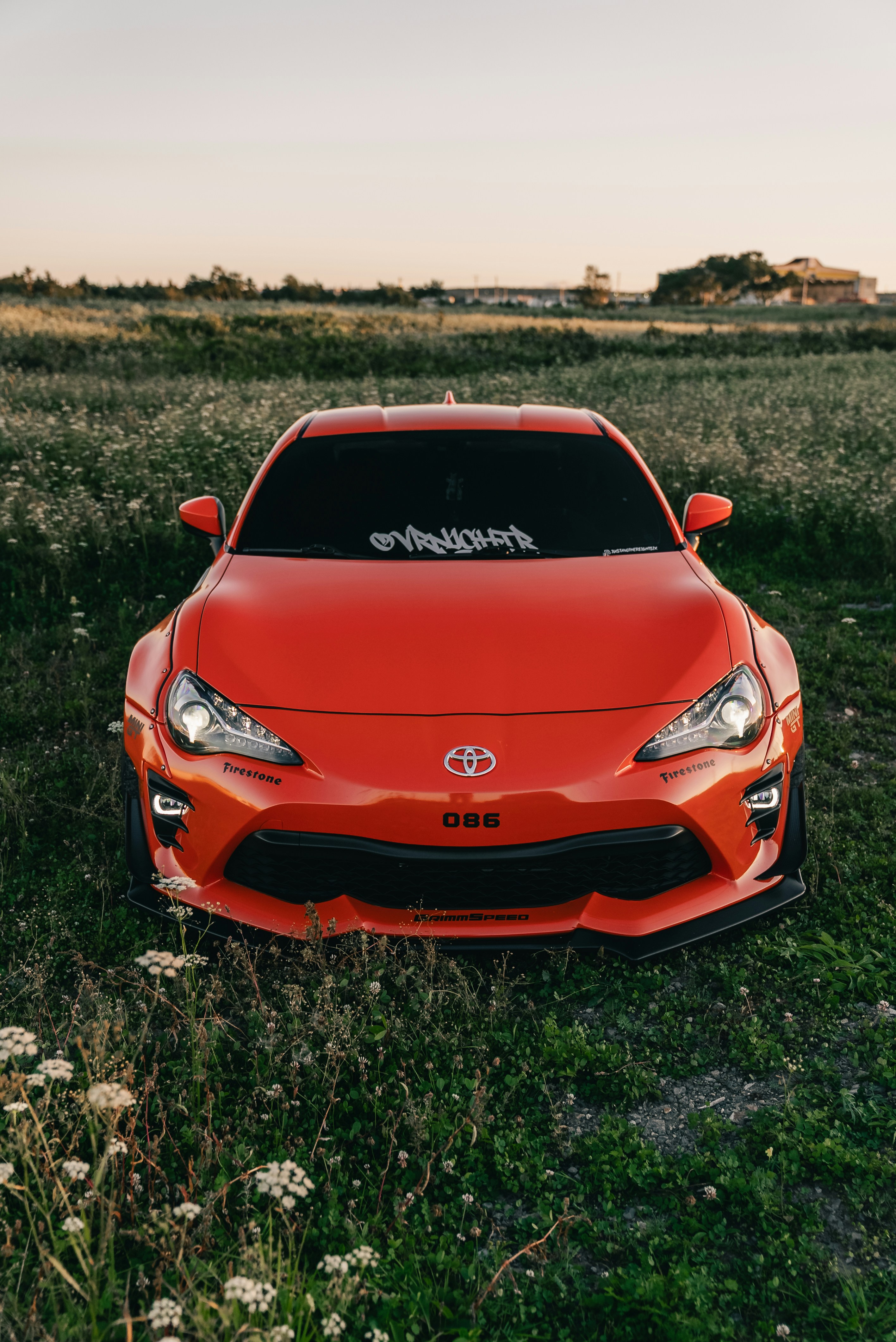 An orange Toyota 86 sports car parked in a grassy field at golden hour