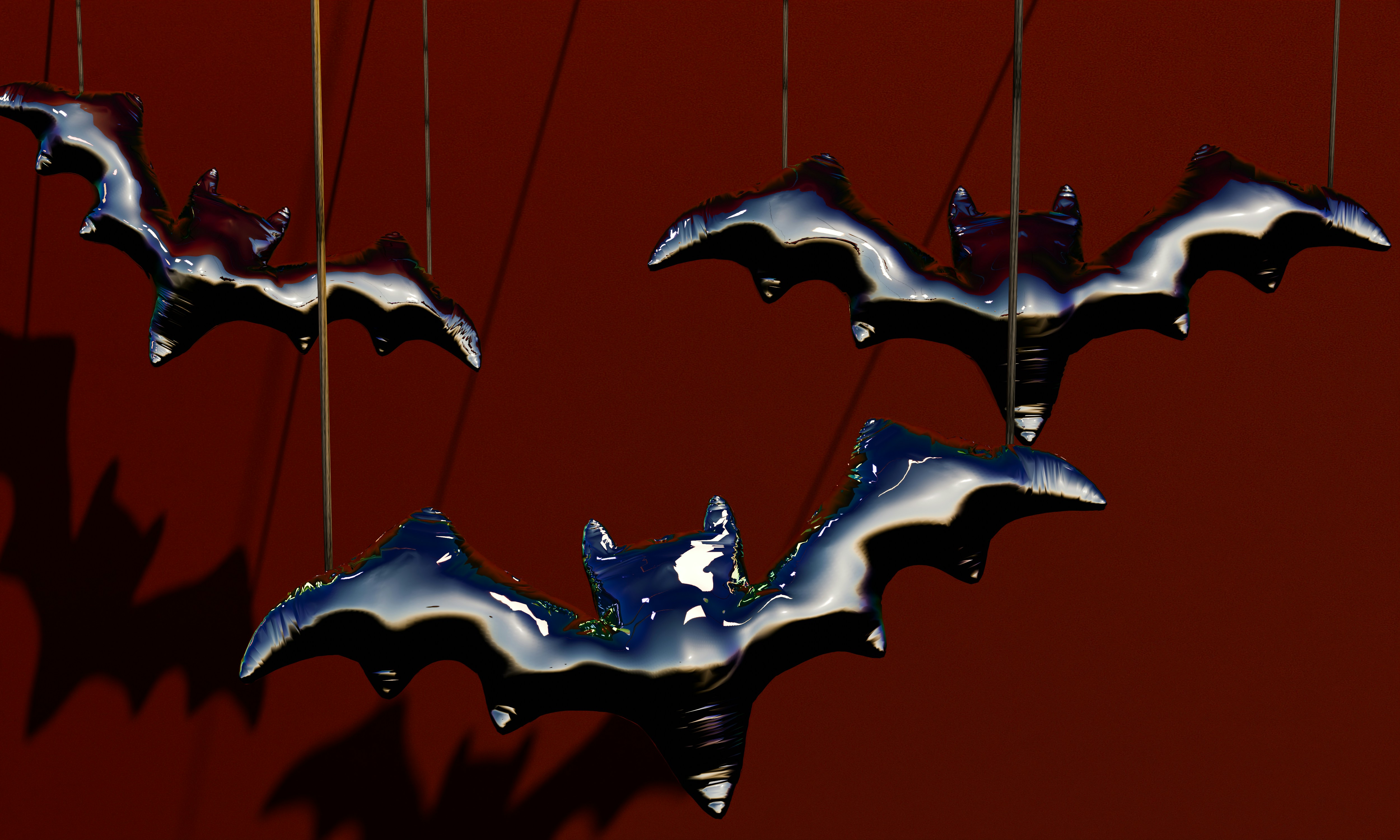 Three shiny black bat-shaped balloons hanging against a dark red background