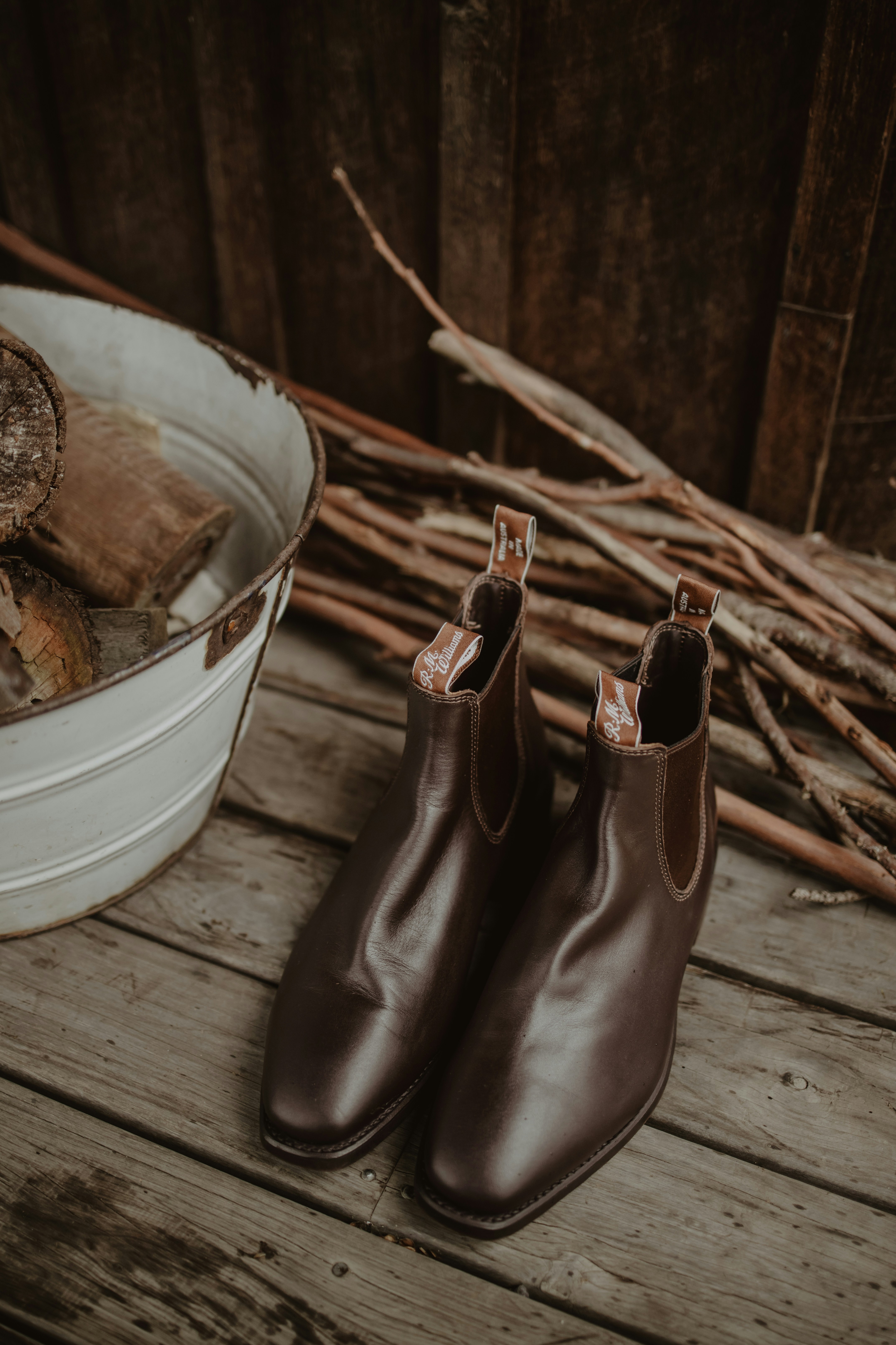 Sepasang sepatu bot Chelsea kulit coklat di atas dek kayu dekat kayu bakar