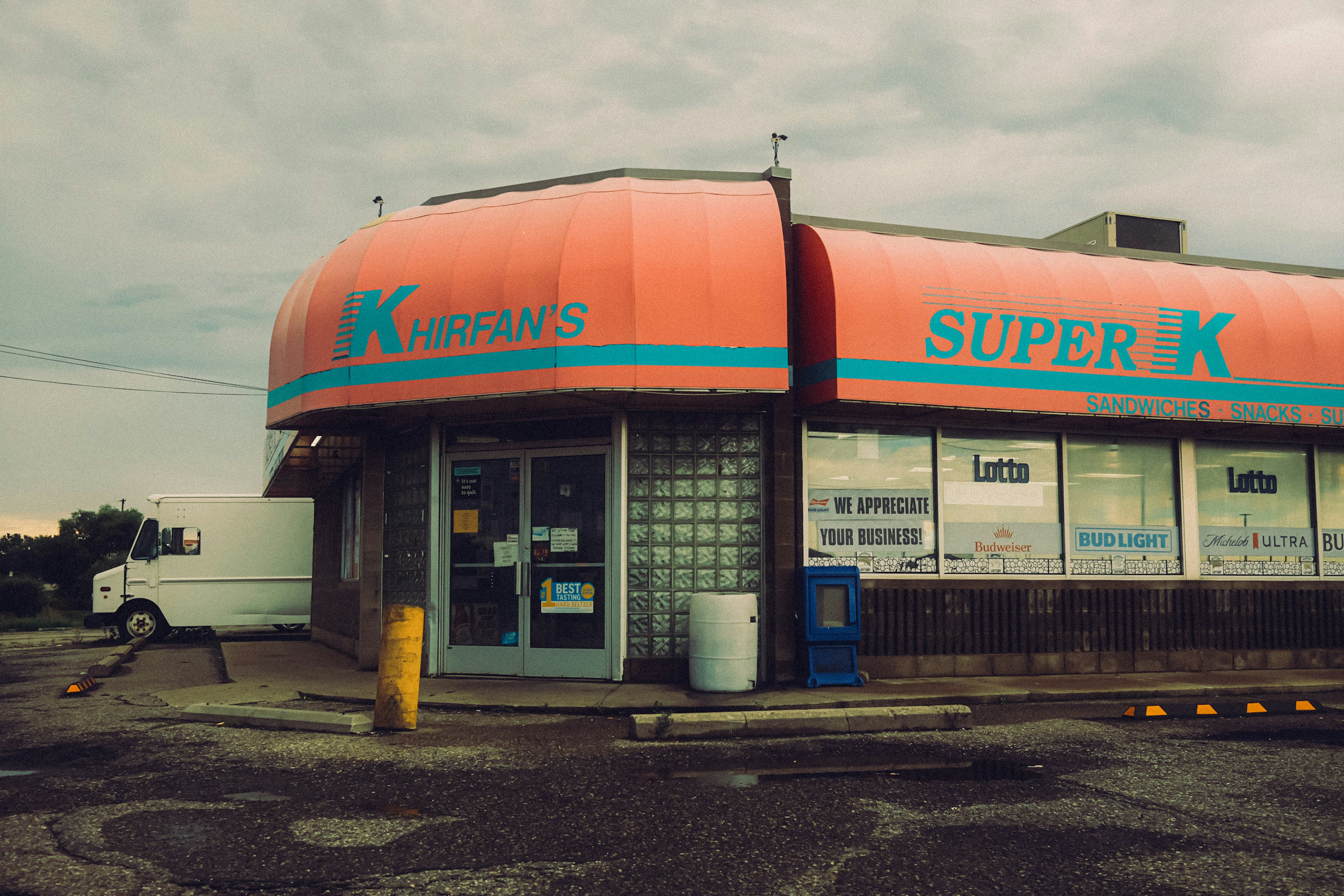 A corner convenience store with a large orange awning and glass block windows