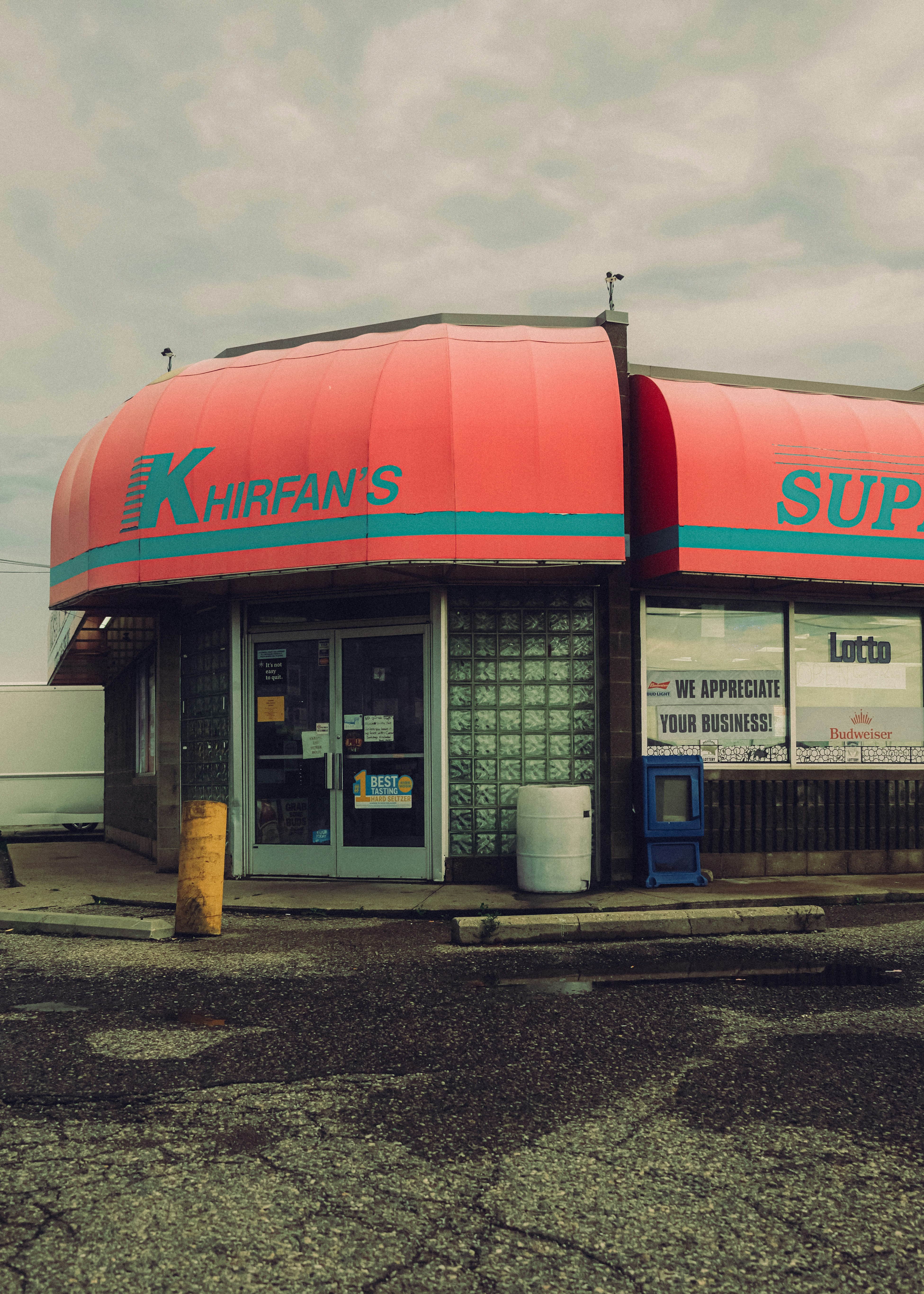 A corner store with a red awning and glass block walls under a cloudy sky