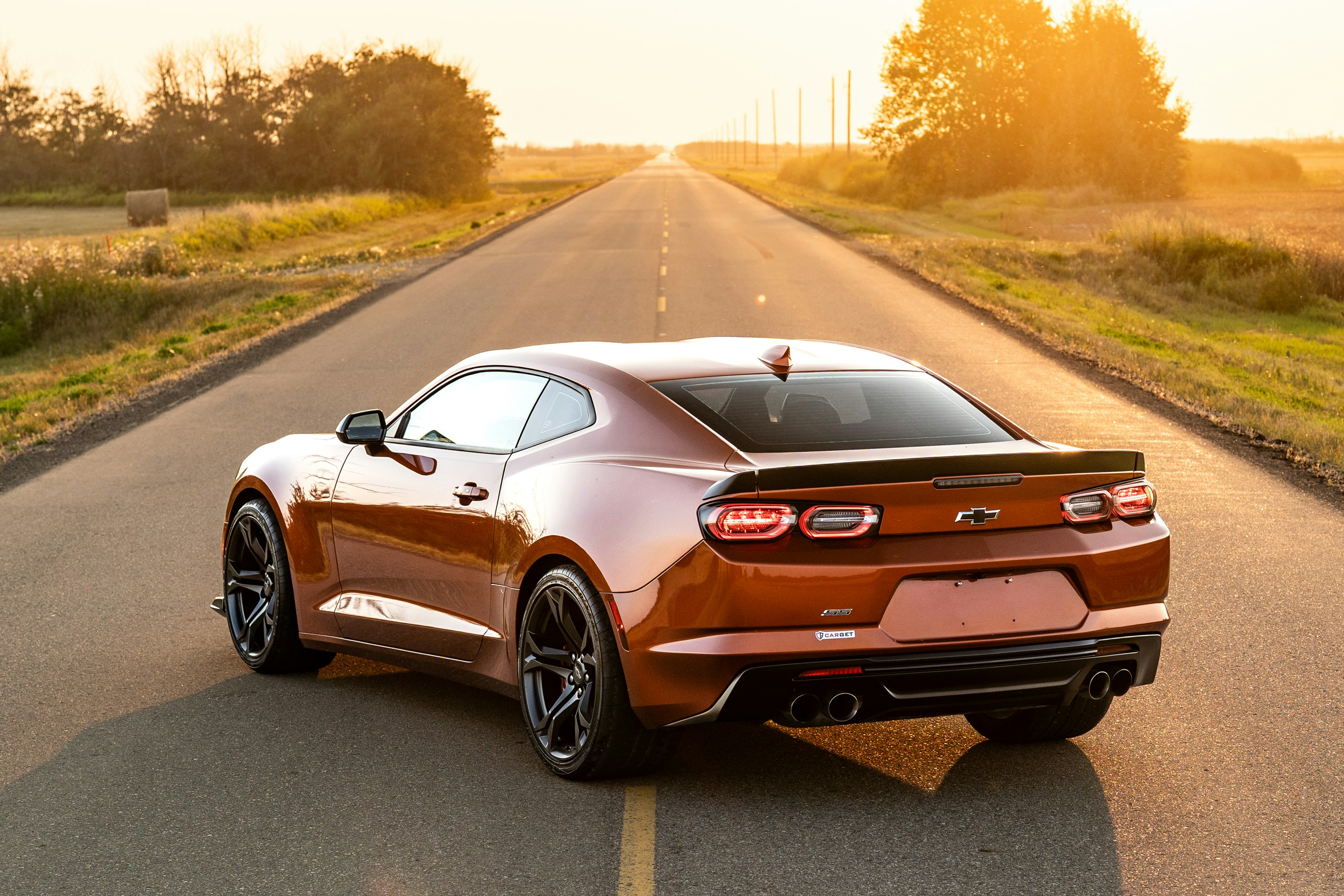 A copper Chevrolet Camaro on a rural road during the golden hour