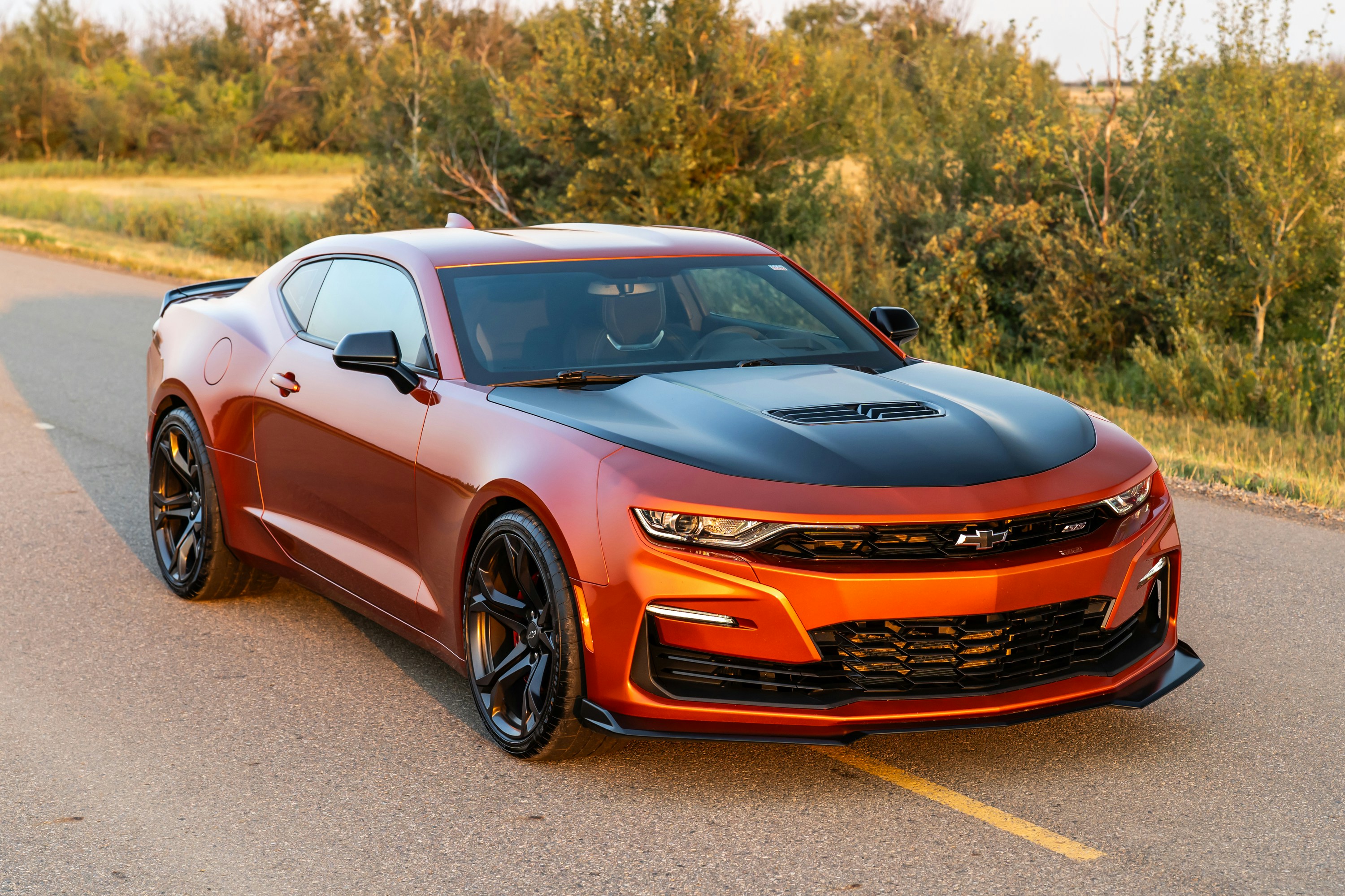 A metallic orange sports car with a black hood on a paved road