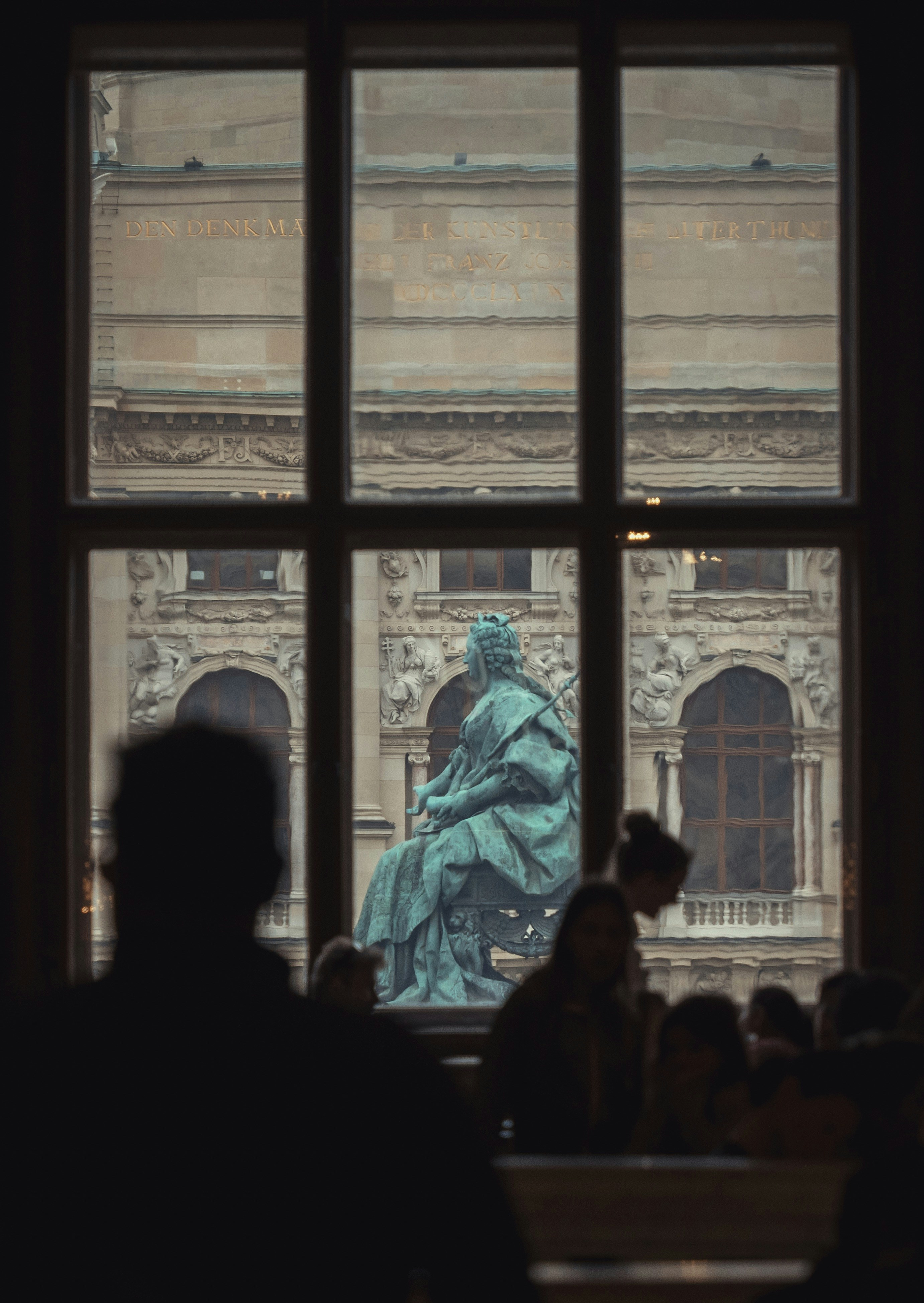 A bronze statue of Maria Theresa seen through a window with silhouetted people