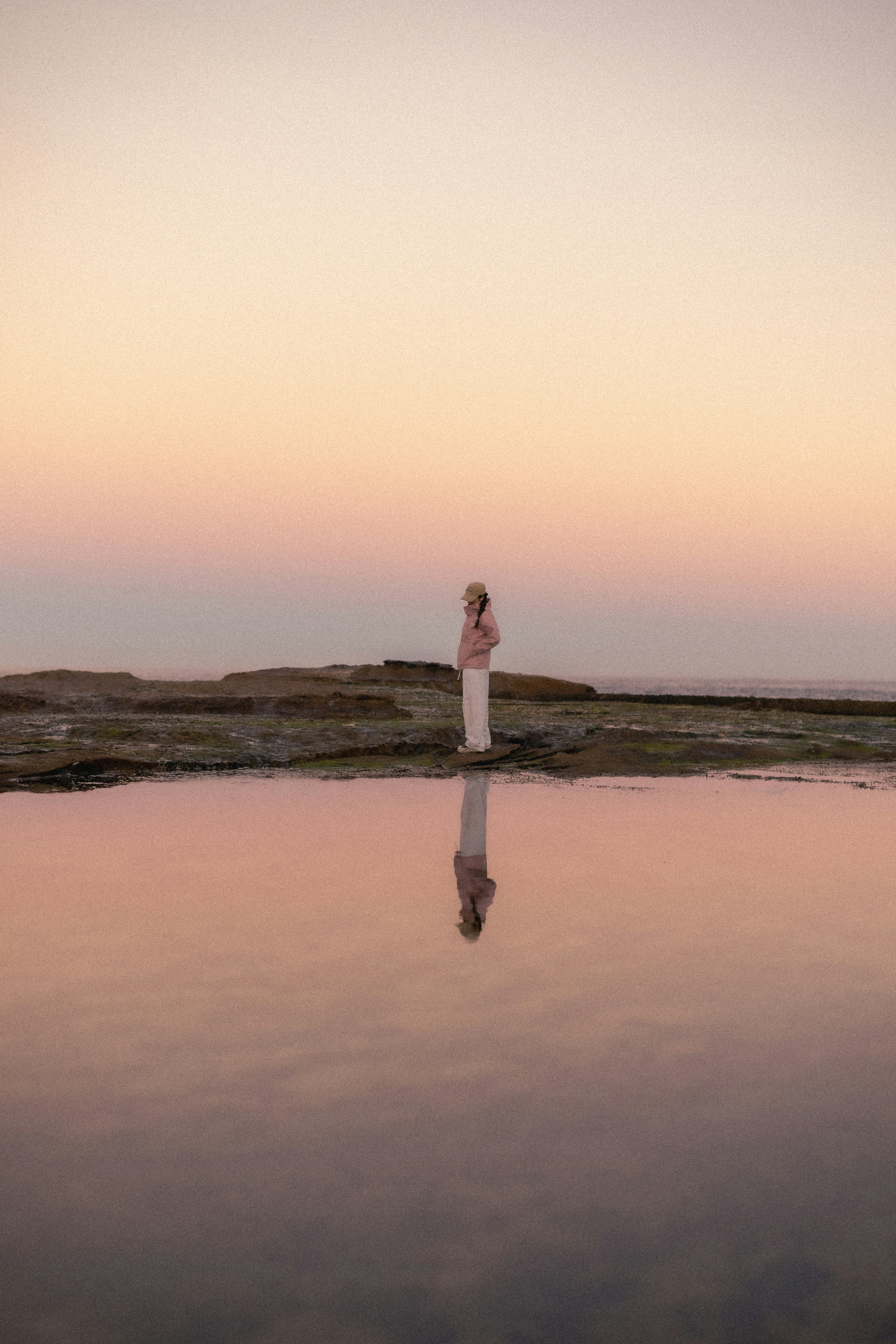 A person in a pink jacket and cap reflected in a calm tide pool - 相关推荐