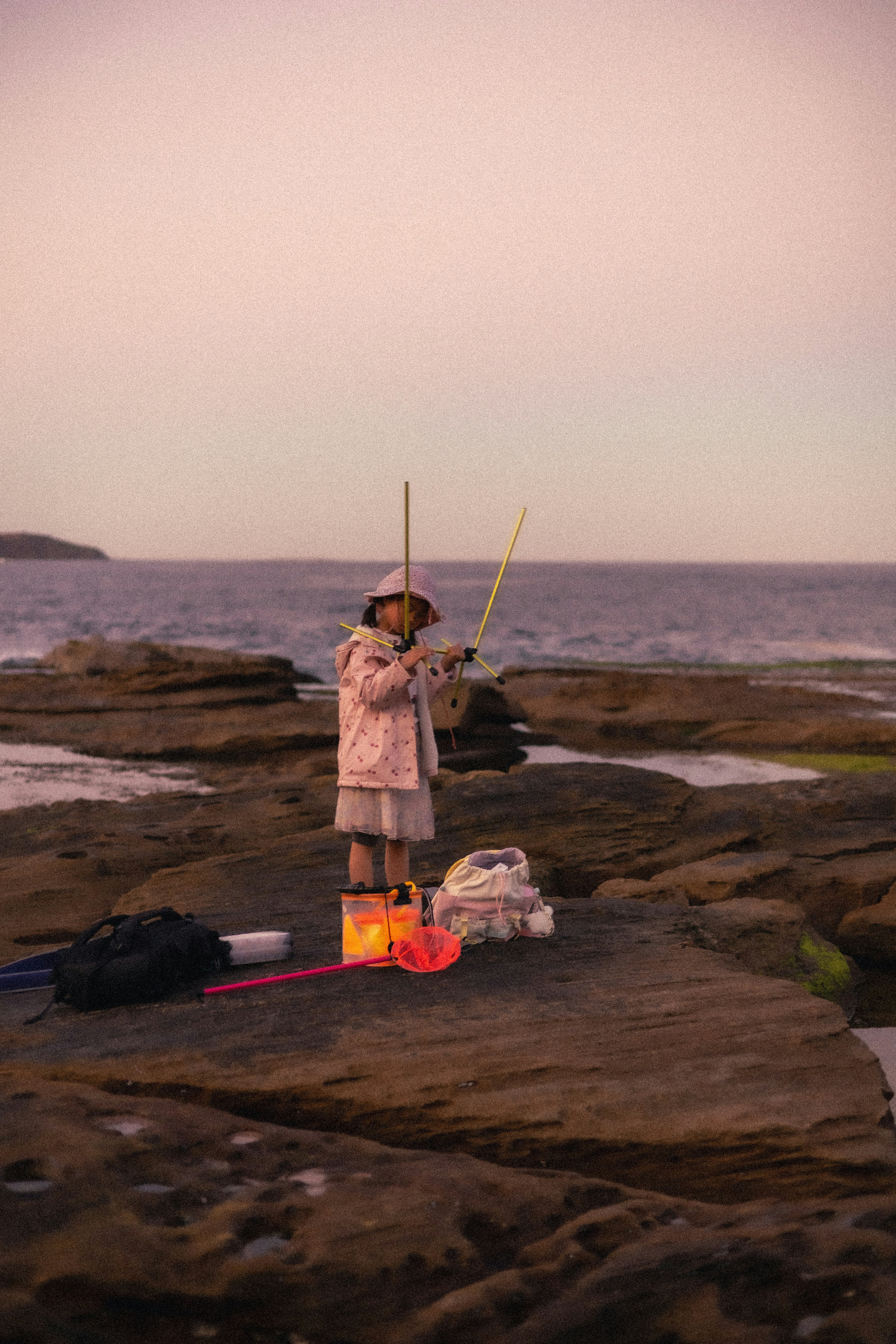 A child in a pink jacket holding a folding stool on a rocky beach