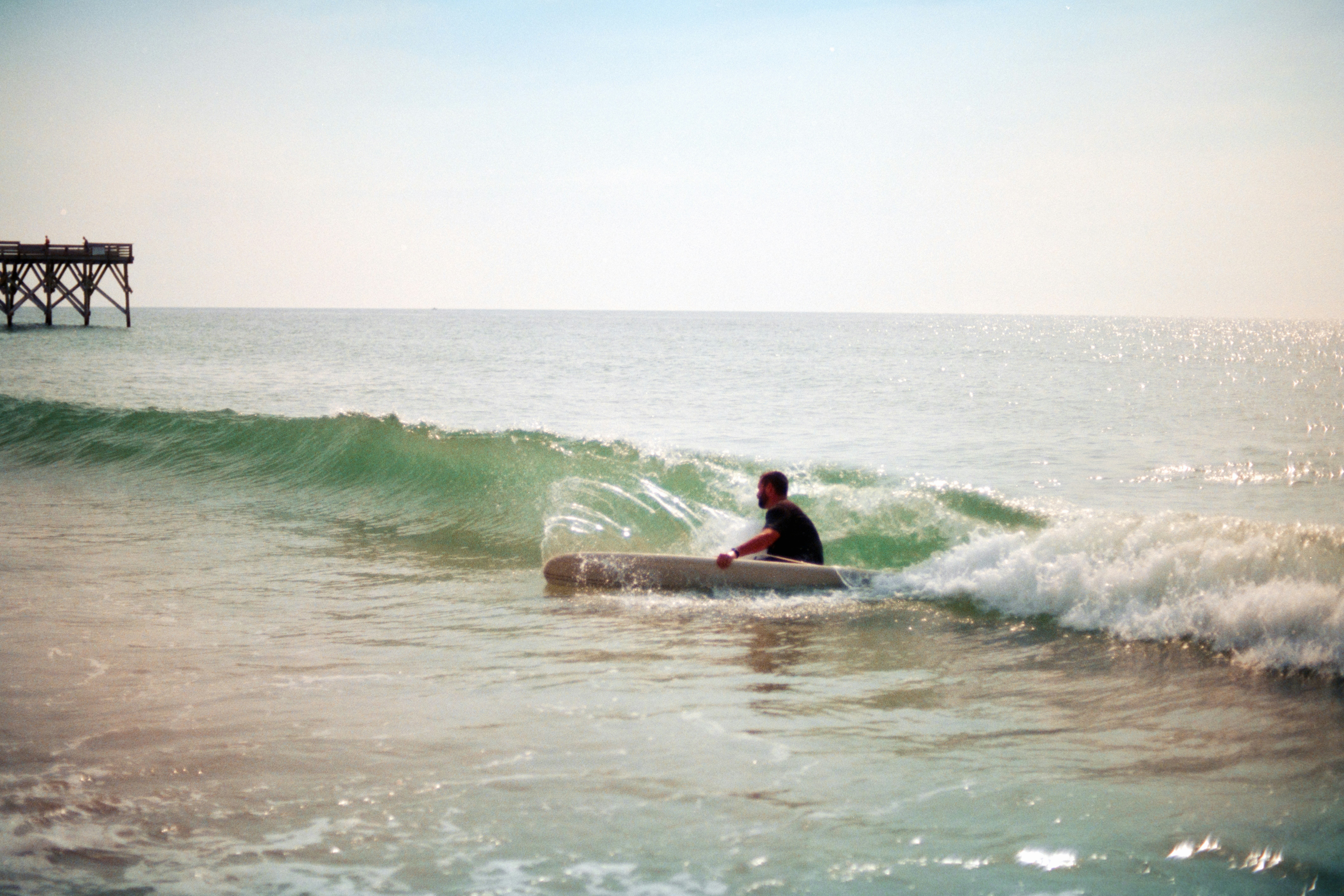 Una persona remando una tabla de surf a través de una pequeña ola rompiendo cerca de un muelle
