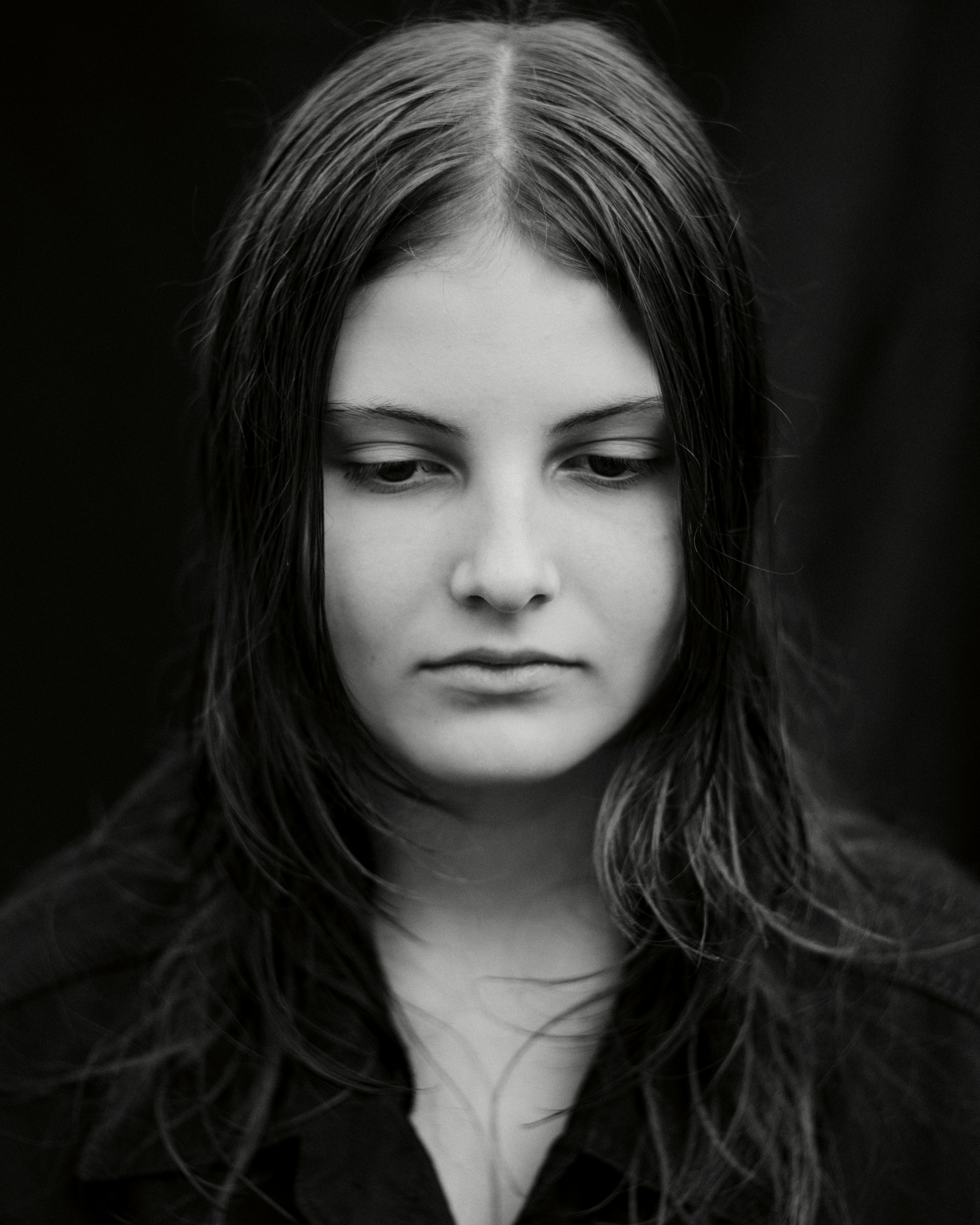 A person with long dark hair looking down against a black background